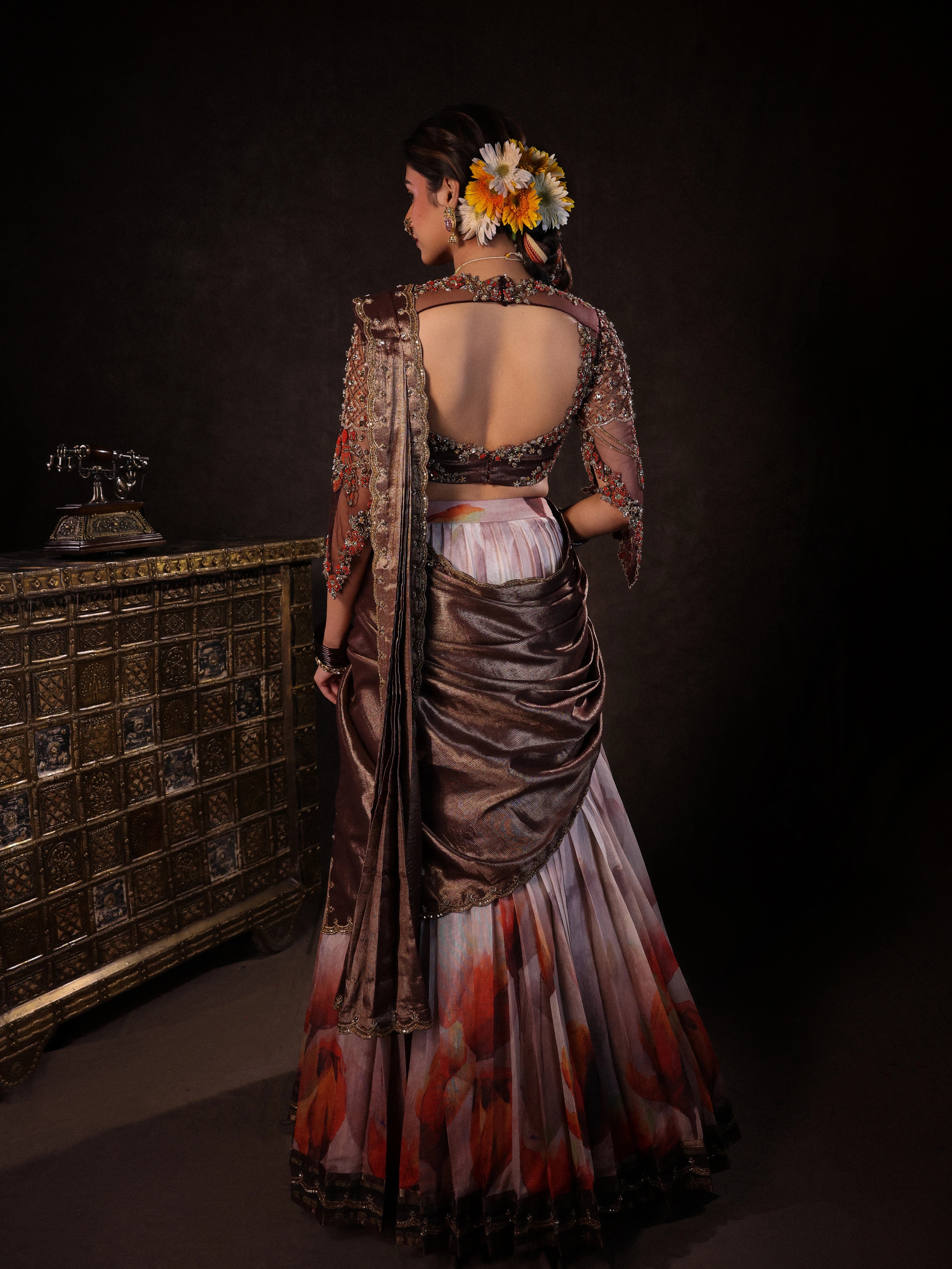 Model Dr Sree Advaita posing for back design in a brown & printed ivory silk half saree set handcrafted with zardozi, resham, cutdana, sequins & rhinestones. Team Archana Karthick completed the style with brown glass bangles, a ring, jhumkas, nose ring and a maang tikka.