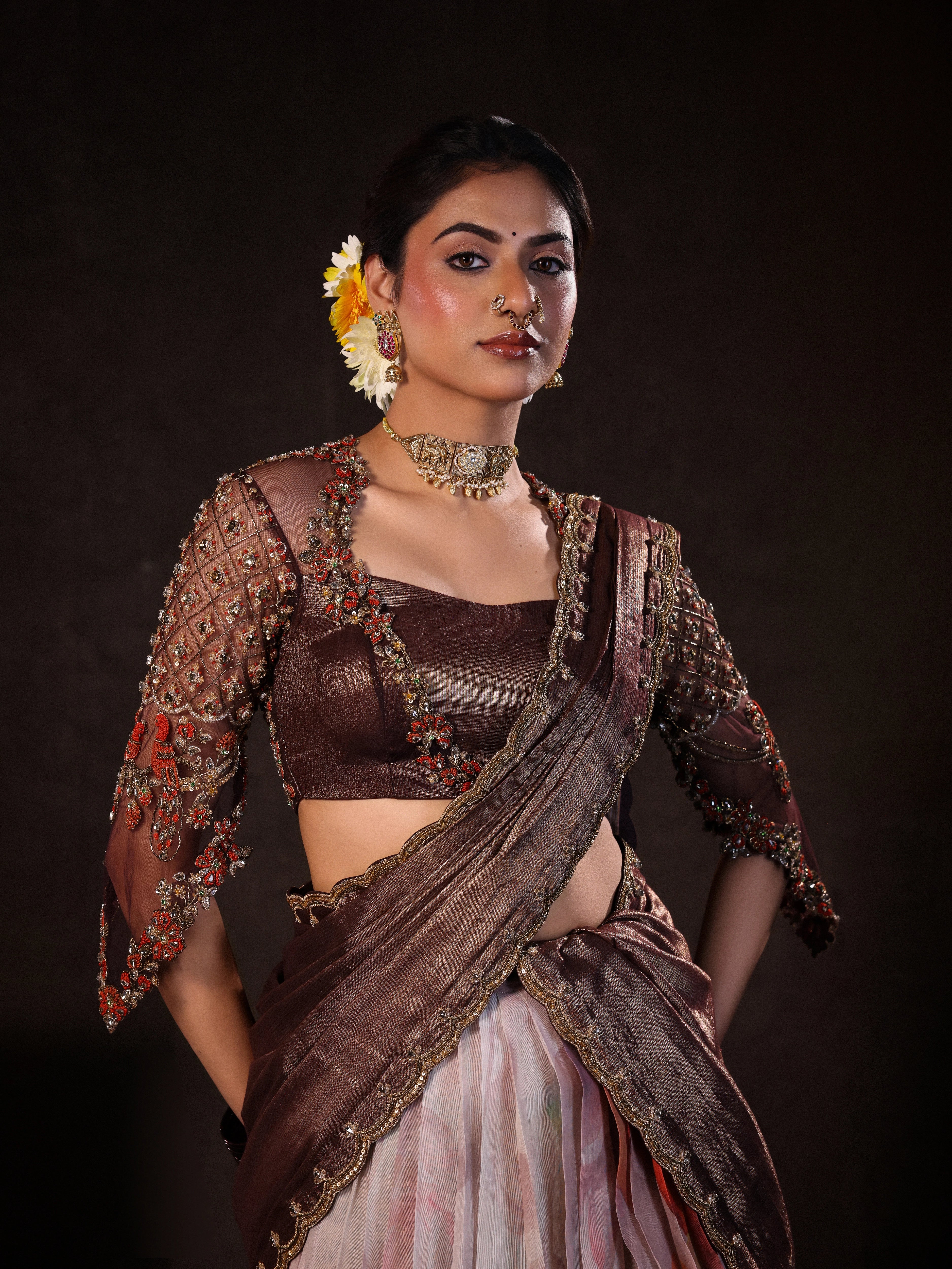 Model Dr Sree Advaita posing for front profile in a brown & printed ivory silk half saree set handcrafted with zardozi, resham, cutdana, sequins & rhinestones. Team Archana Karthick completed the style with brown glass bangles, a ring, jhumkas, nose ring and a maang tikka.