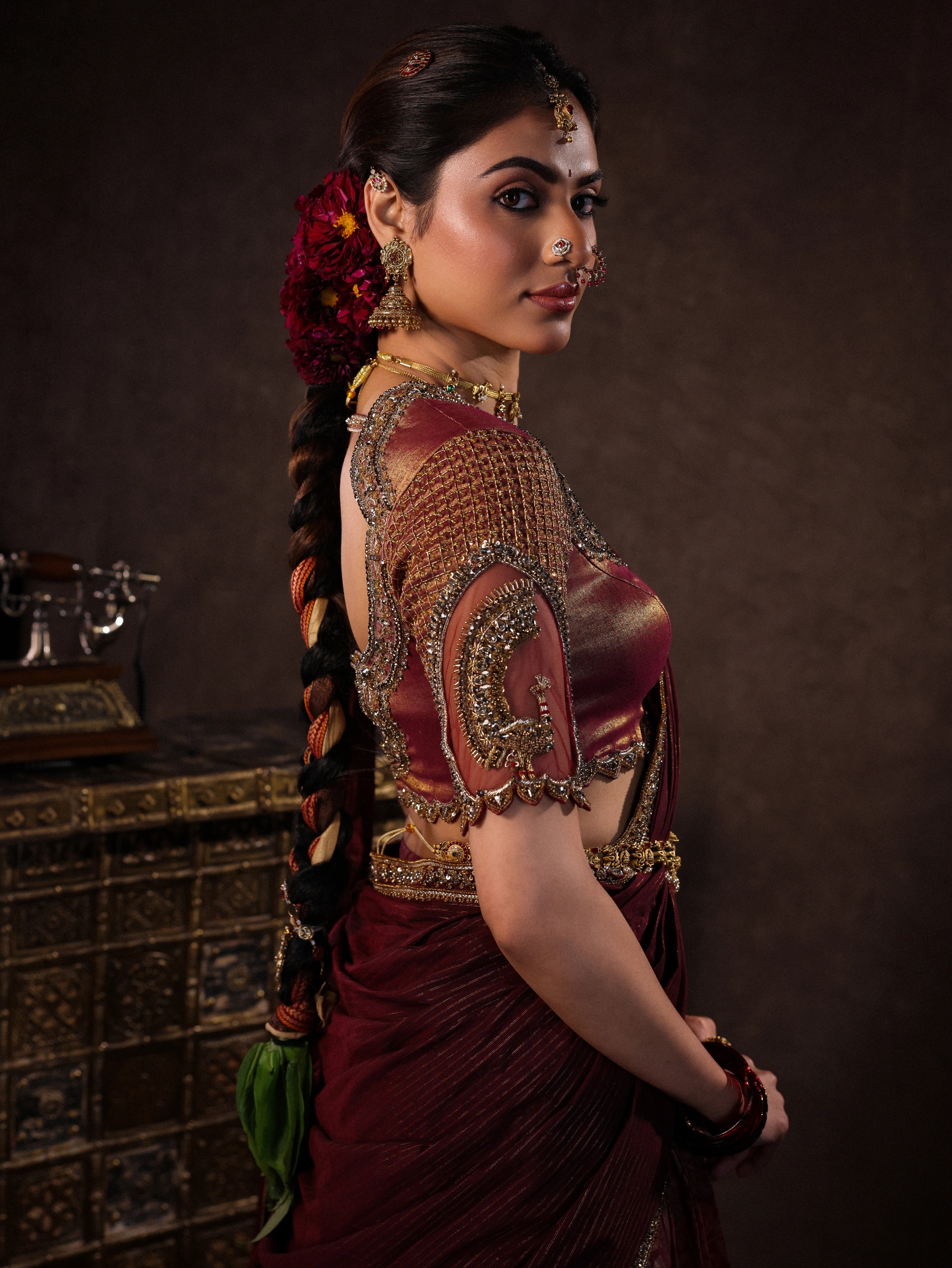 Model Dr Sree Advaita posing in a brownish maroon silk half saree set intricately handcrafted with zardozi, resham, cutdana, sequins & rhinestones. Team Archana Karthick completed the style with maroon glass bangles, a ring, jhumkas, nose ring and a maang tikka.