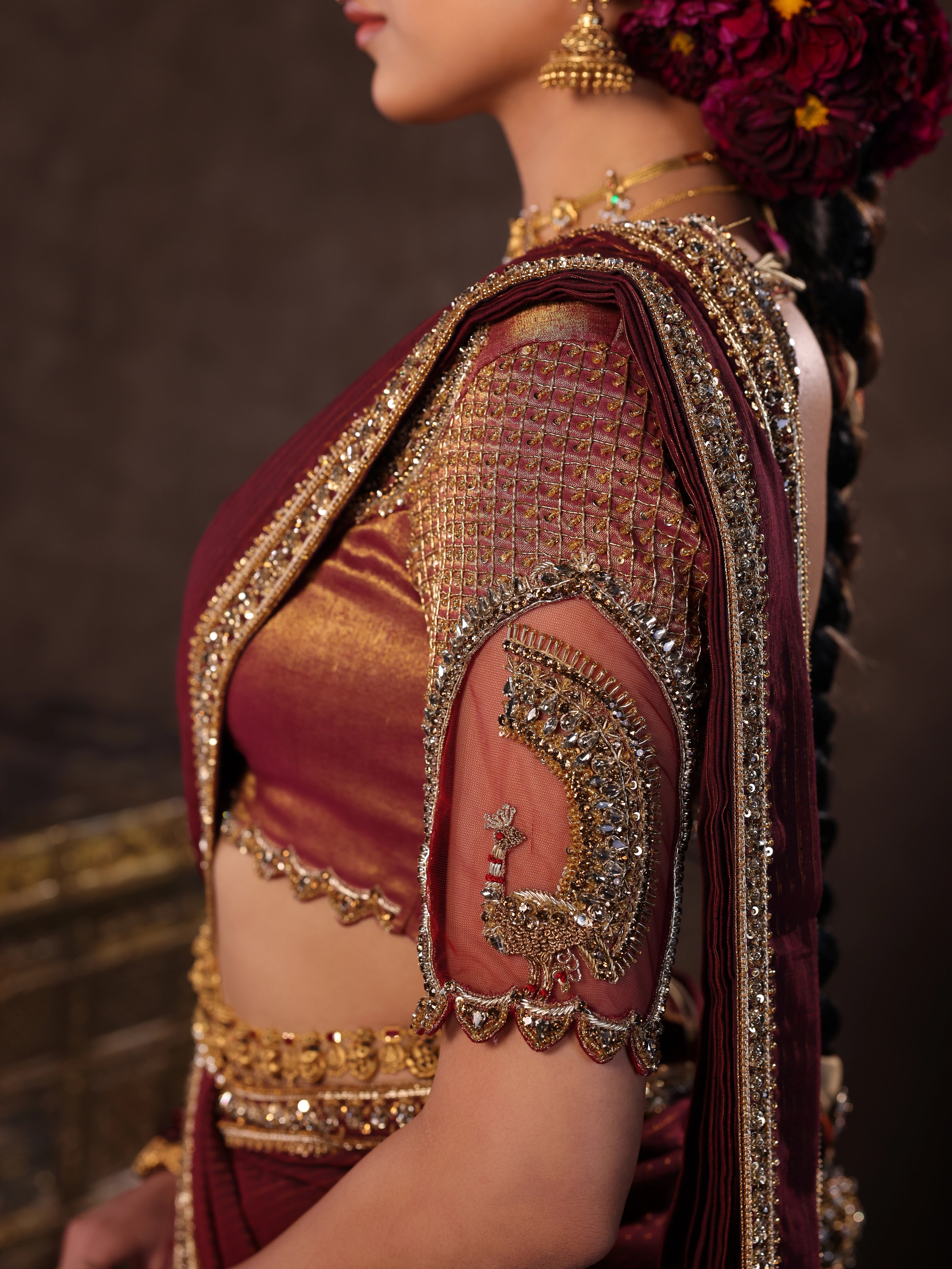 Model Dr Sree Advaita showcasing sleeve in a brownish maroon silk half saree set intricately handcrafted with zardozi, resham, cutdana, sequins & rhinestones. Team Archana Karthick completed the style with maroon glass bangles, a ring, jhumkas, nose ring and a maang tikka.