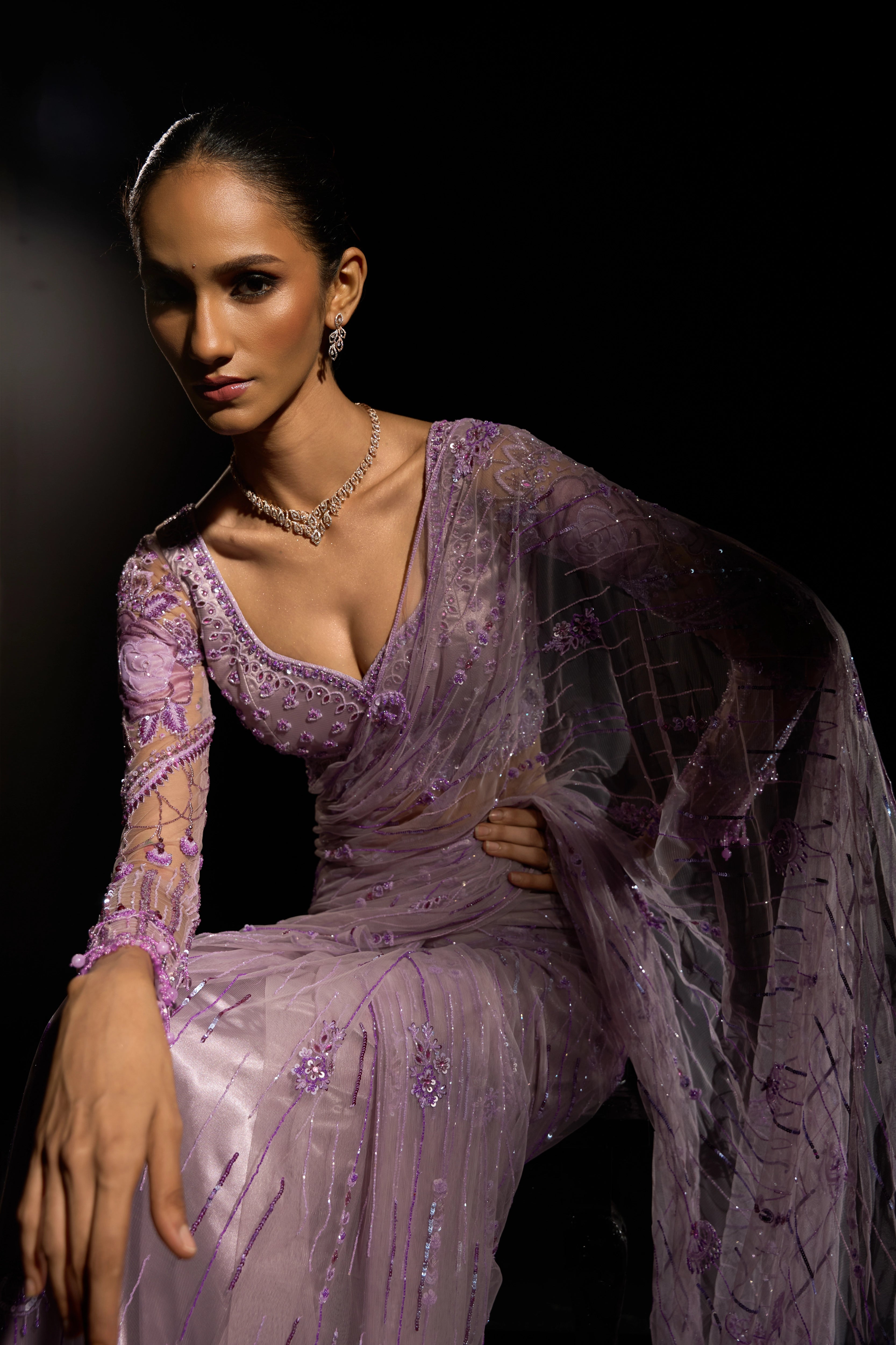 Model Esha Gohil posing seated in a lavender saree set intricately adorned with sequins, rhinestones, crystals and cutdana for "STARDUST" - A/W'25 saree collection by team Archana Karthick.