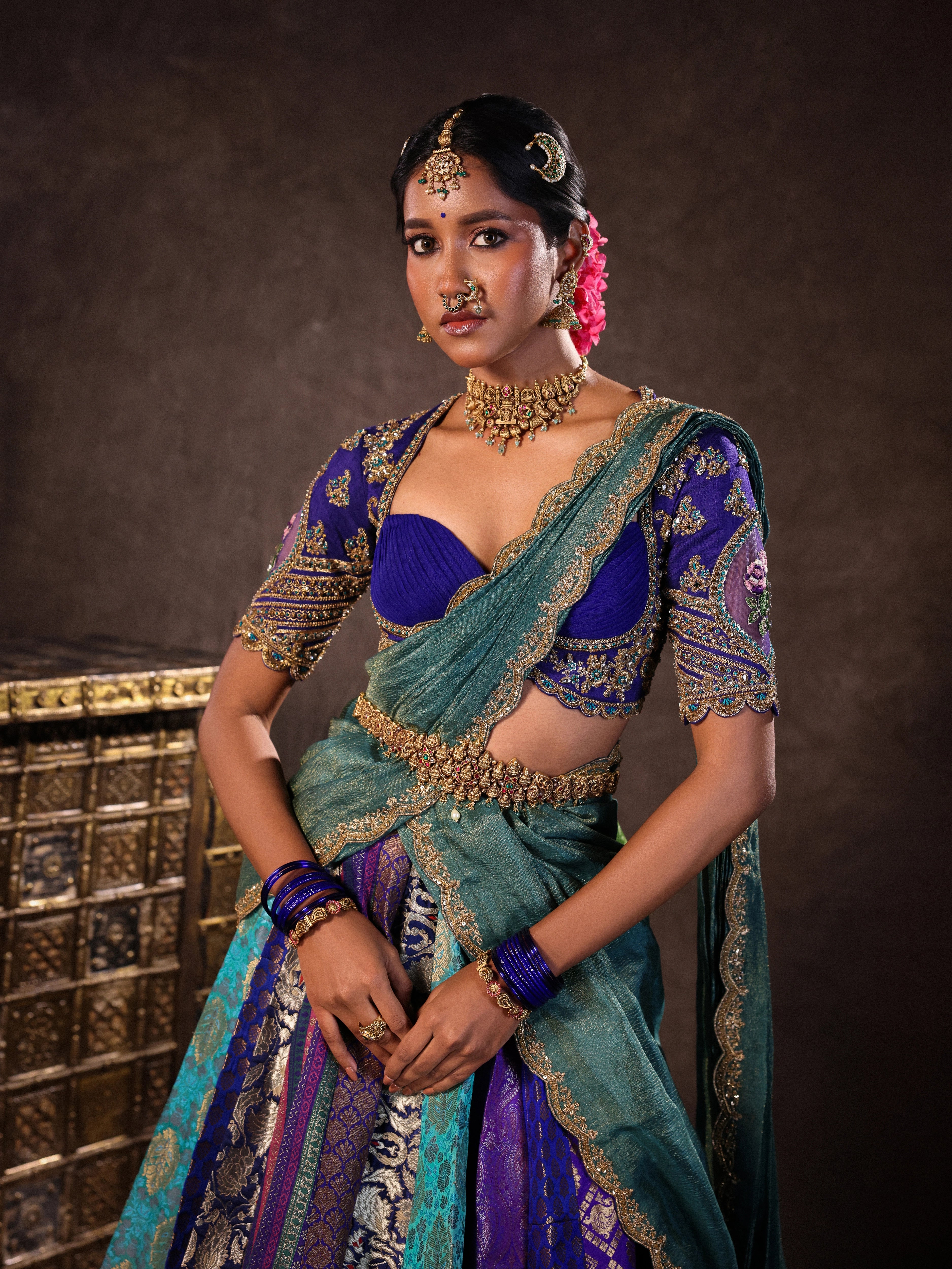 Model Gayathri Dhanasekar during photoshoot in a brocade, raw silk and tissue silk half saree set in shades of blue handcrafted with zardozi, resham, sequins and rhinestones. Team Archana Karthick completed the style with blue glass bangles, a ring, a choker, jhumkas, nose ring and a maang tikka.