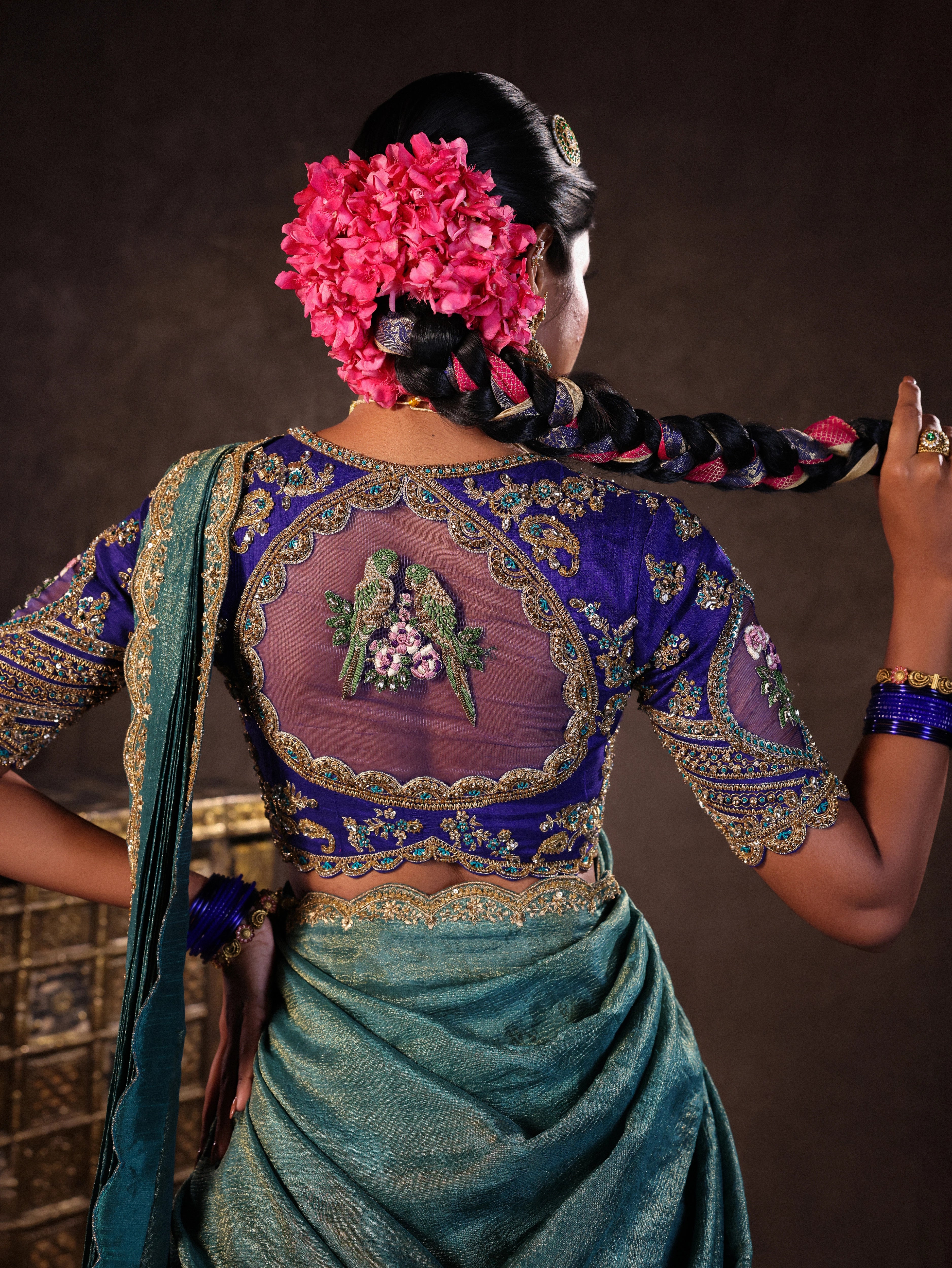 Model Gayathri Dhanasekar posing for back blouse design in a brocade, raw silk and tissue silk half saree set in shades of blue handcrafted with zardozi, resham, sequins and rhinestones. Team Archana Karthick completed the style with blue glass bangles, a ring, a choker, jhumkas, nose ring and a maang tikka.