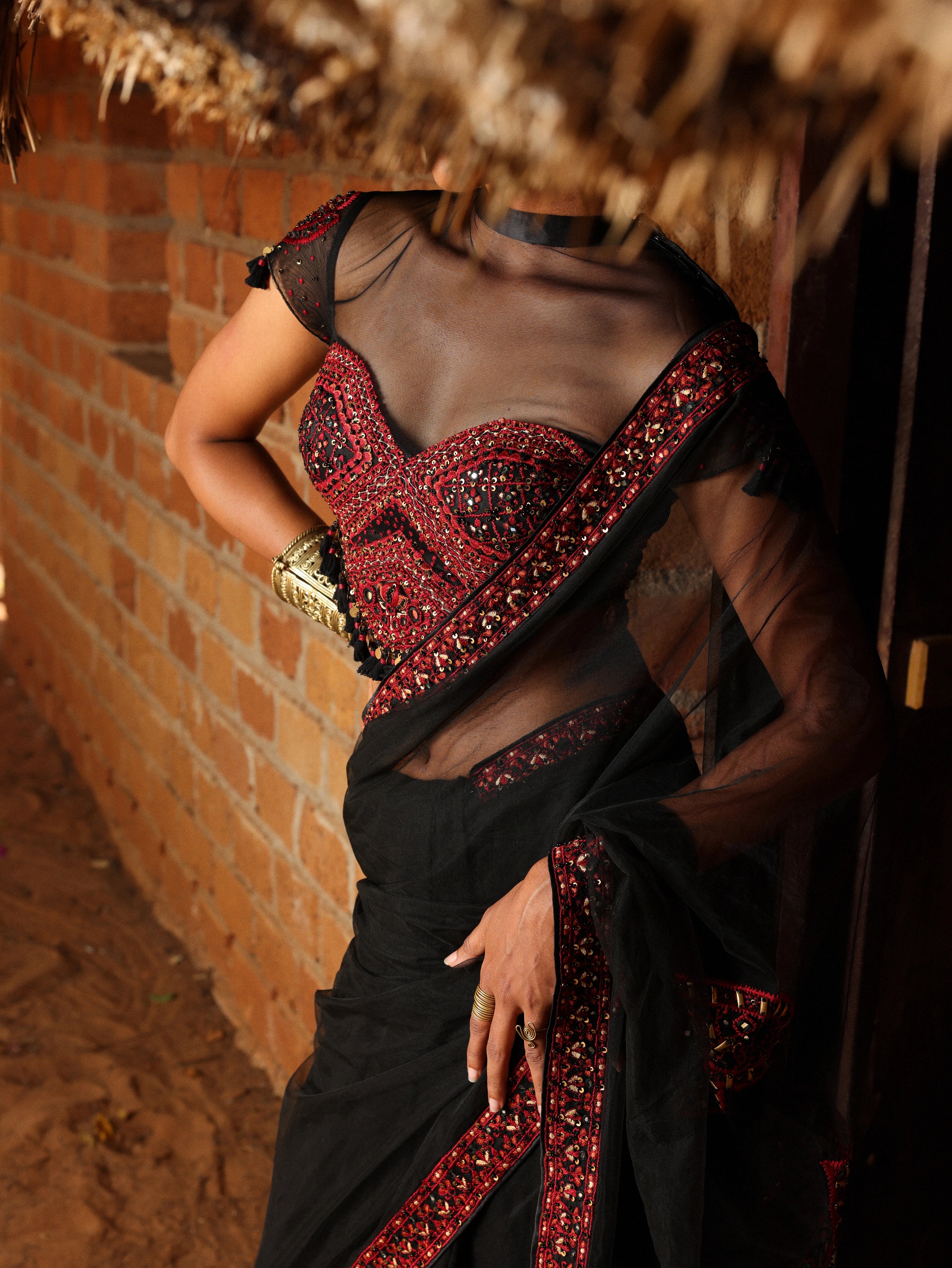 Model Gayathri Dhanasekar posing for blouse front design in a black net saree with a back full neck blouse & sweetheart neckline. It is handcrafted with red resham & french knot work by team Archana Karthick.