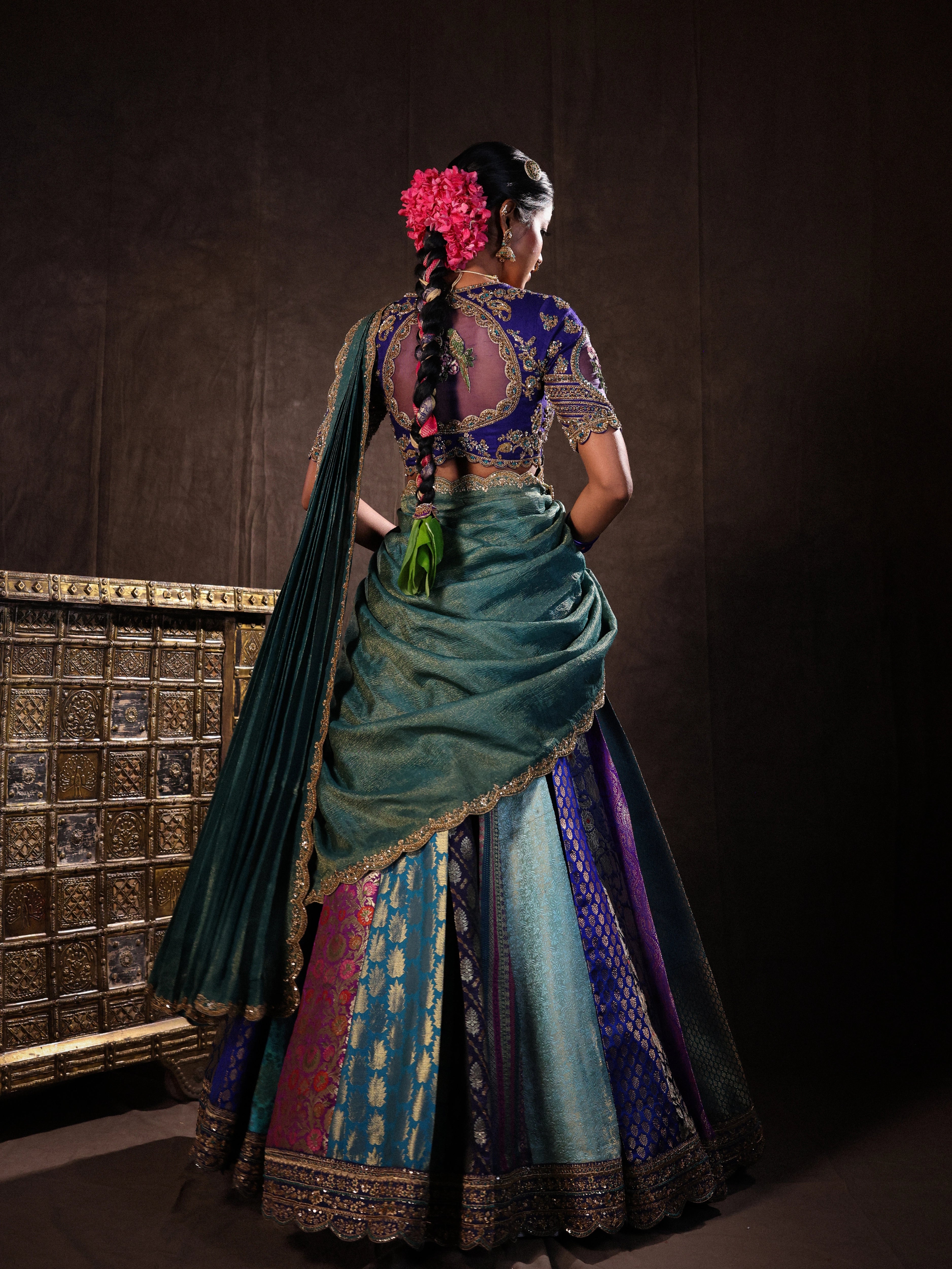 Model Gayathri Dhanasekar showcasing back design in a brocade, raw silk and tissue silk half saree set in shades of blue handcrafted with zardozi, resham, sequins and rhinestones. Team Archana Karthick completed the style with blue glass bangles, a ring, a choker, jhumkas, nose ring and a maang tikka.