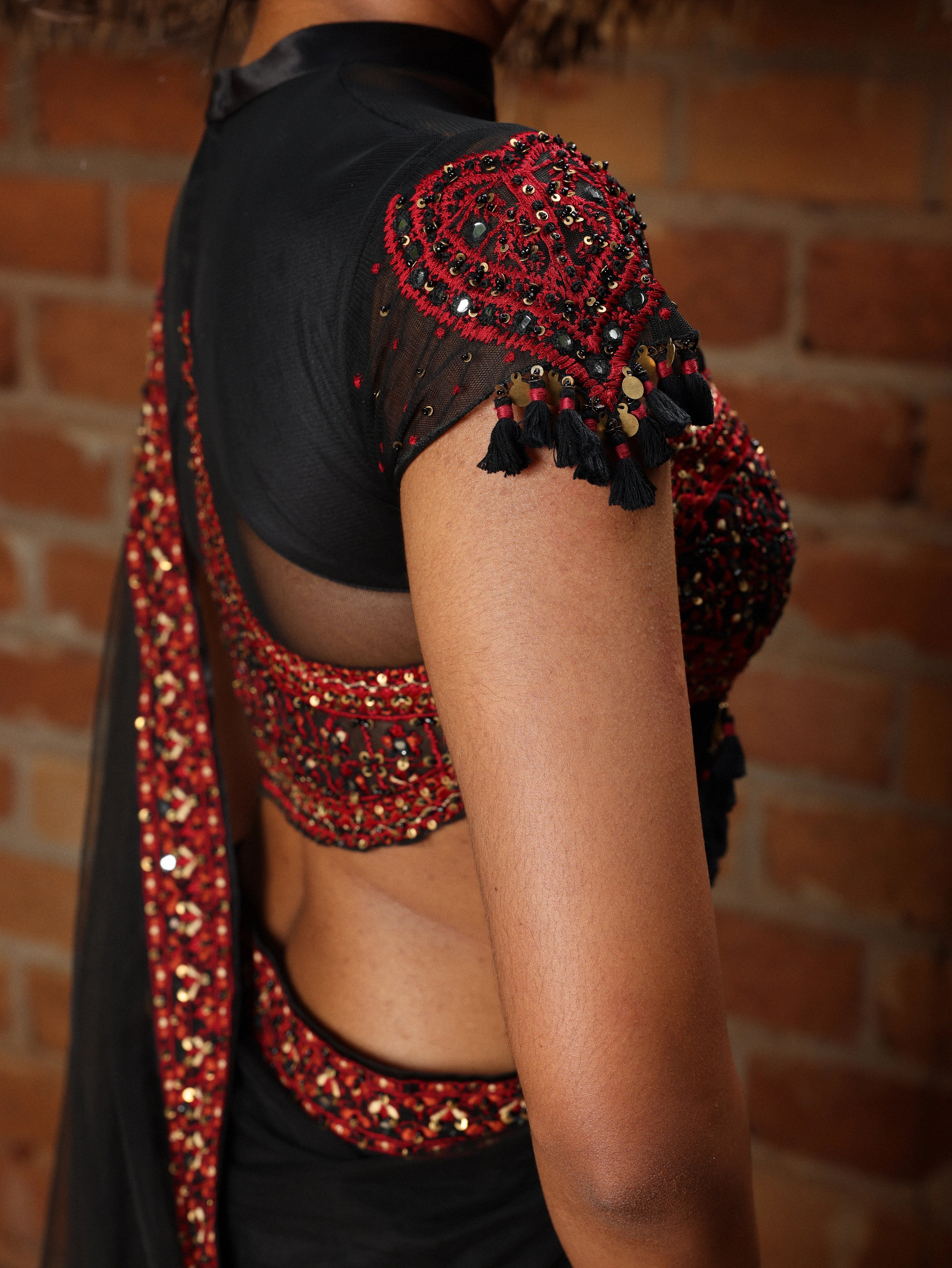 Model Gayathri Dhanasekar showcasing blouse sleeve design in a black net saree with a back full neck blouse & sweetheart neckline. Handcrafted with red resham & french knot work by team Archana Karthick.
