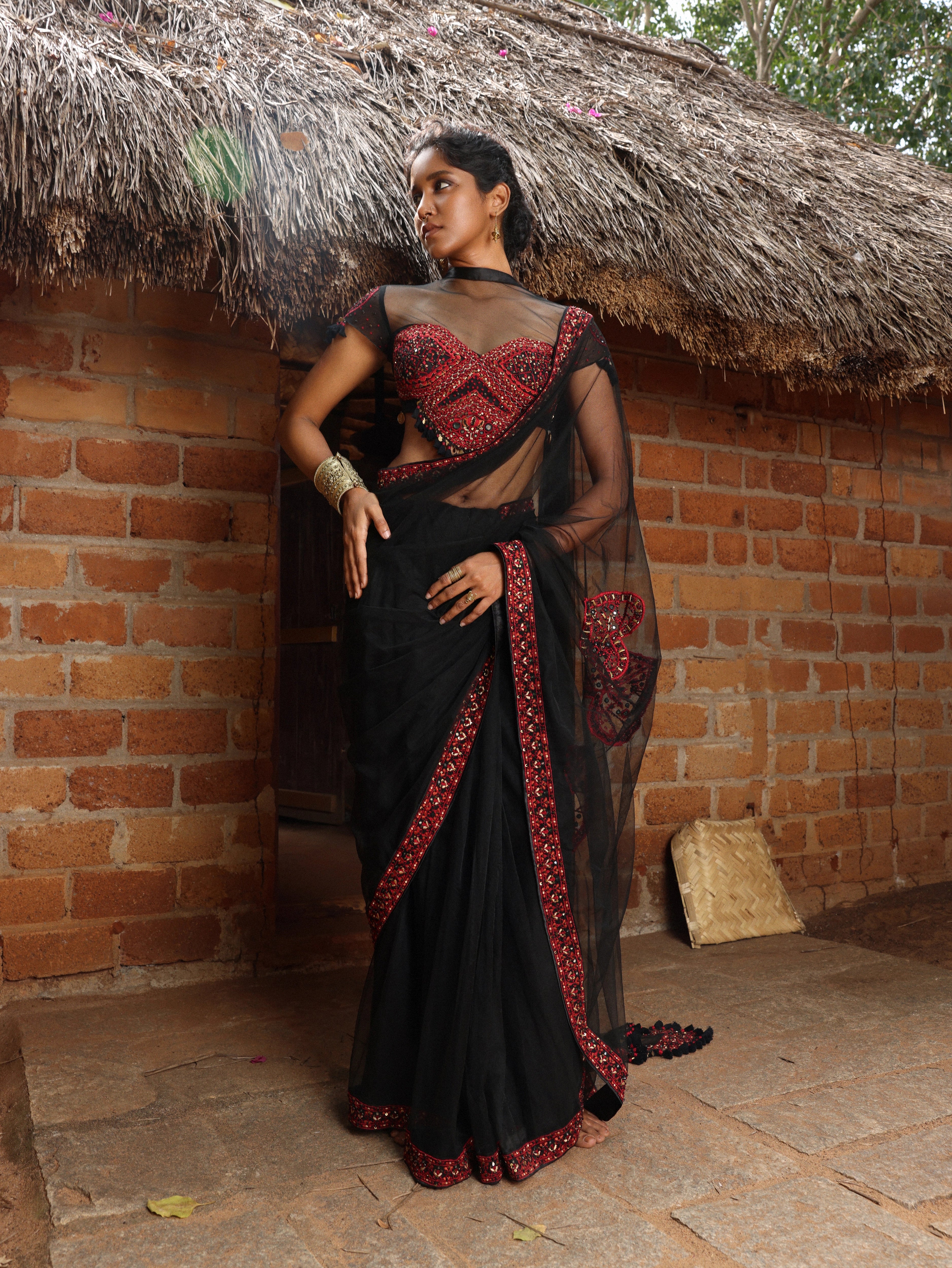 Model Gayathri Dhanasekar showcasing front profile in a black net saree with a back full neck blouse & sweetheart neckline. Handcrafted with red resham & french knot work by team Archana Karthick.