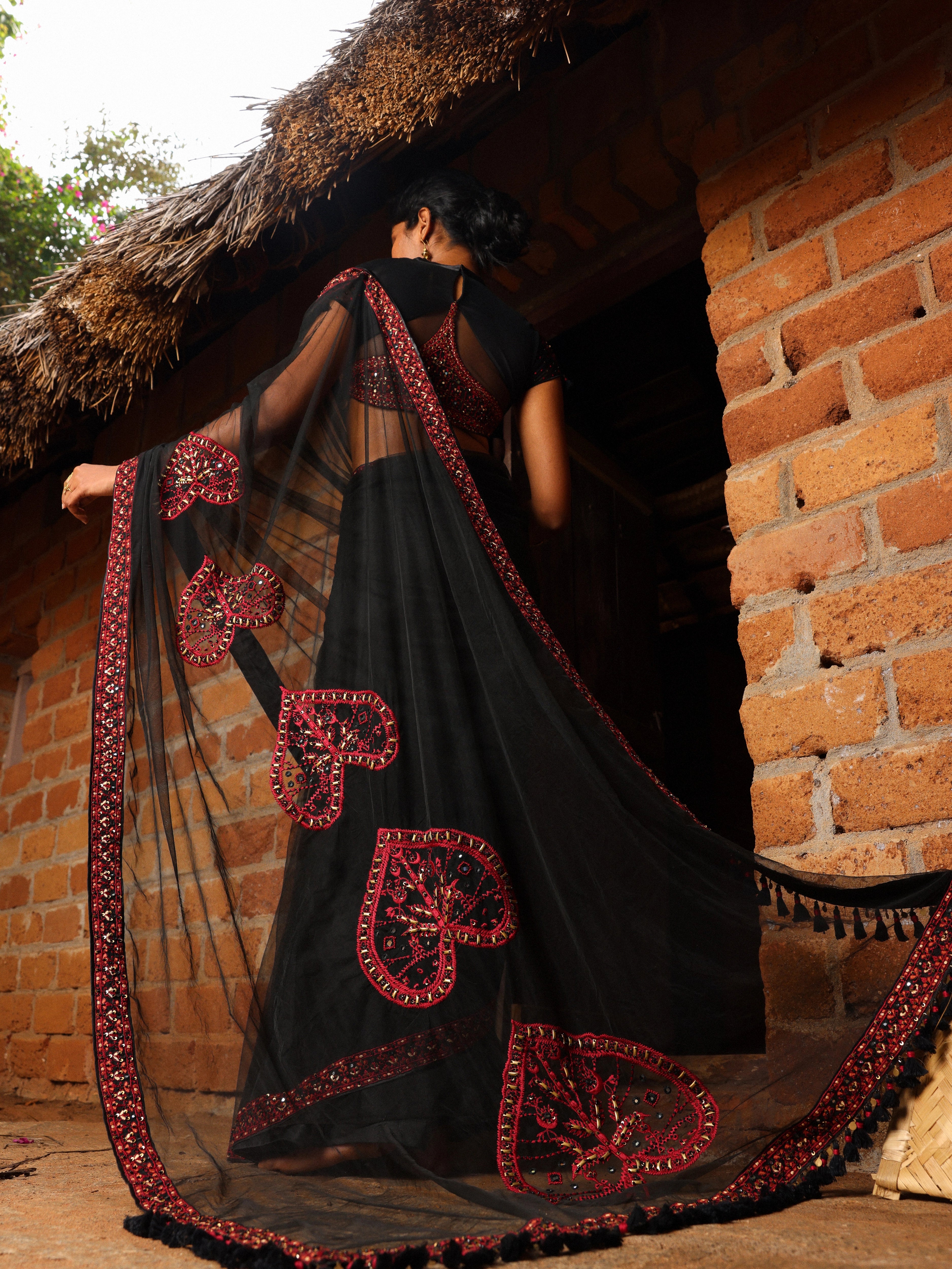 Model Gayathri Dhanasekar showcasing saree pallu design in a black net saree with a back full neck blouse & sweetheart neckline. Handcrafted with red resham & french knot work by team Archana Karthick.