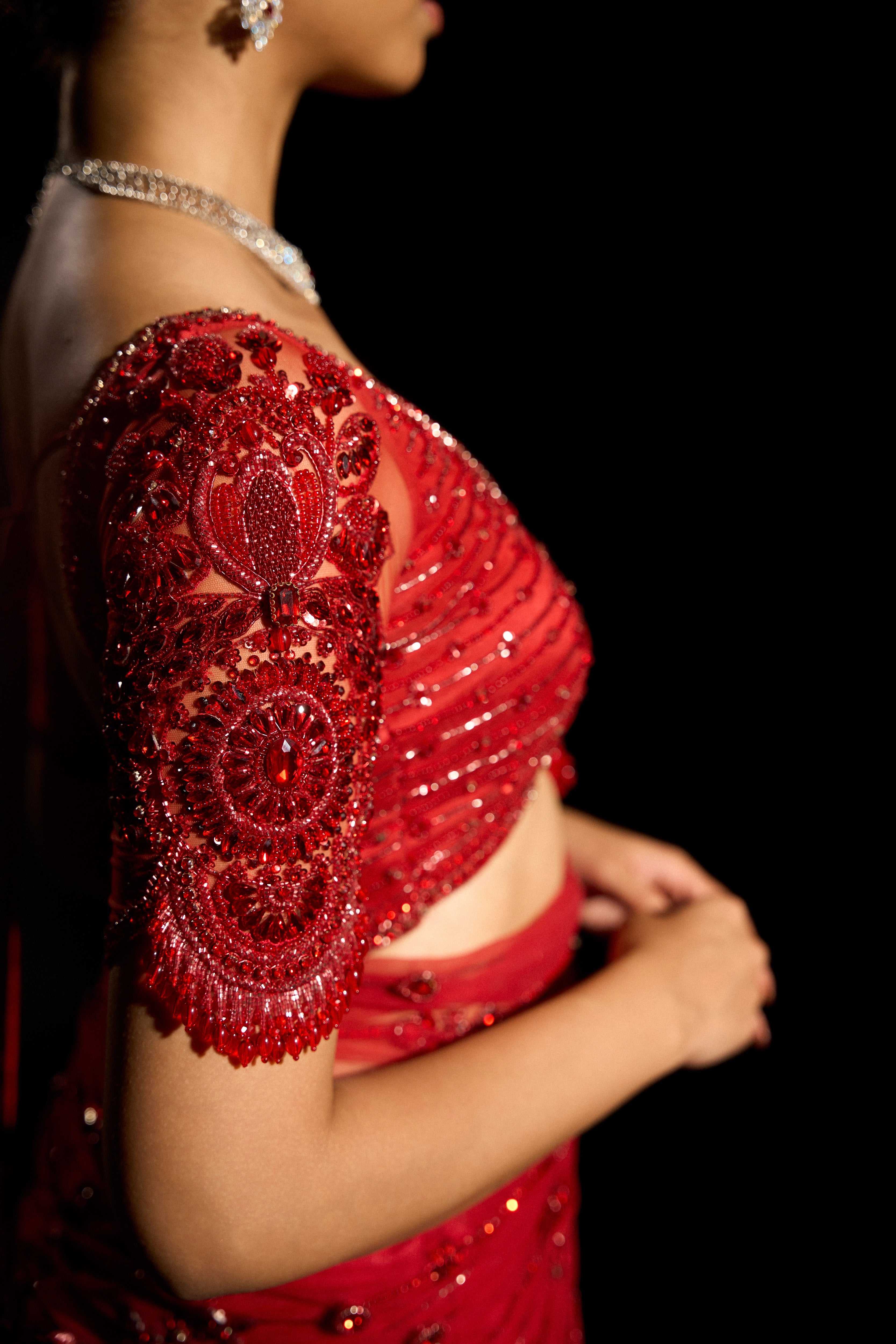 Model Jane C Thompson showcasing blouse sleeve design in a red saree set intricately adorned with sequins, rhinestones, crystals and cutdana for "STARDUST" - A/W'25 saree collection by team Archana Karthick.