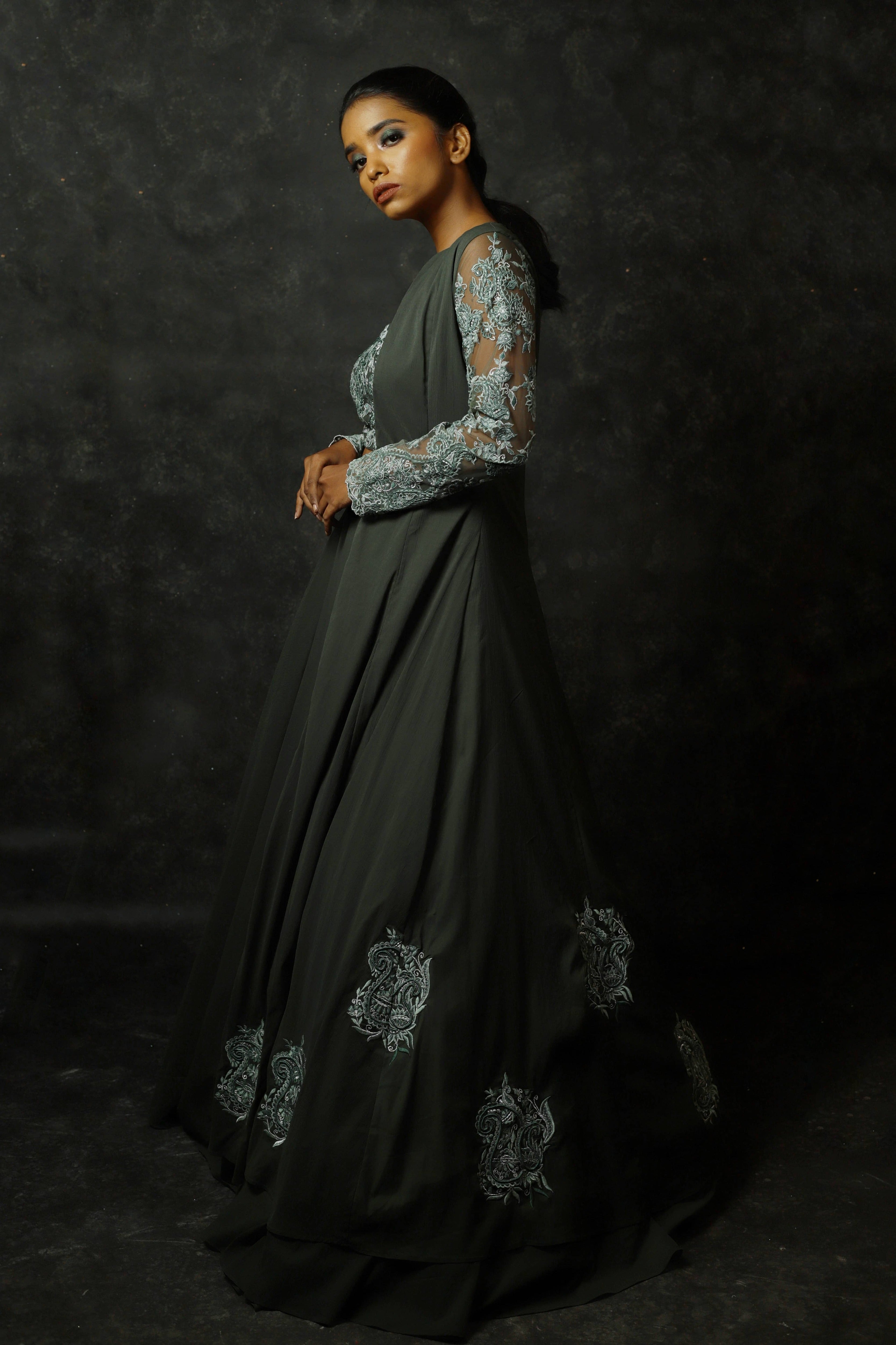 Model Posing sideways in an olive green georgette masakali lehenga with long shrug and bralette