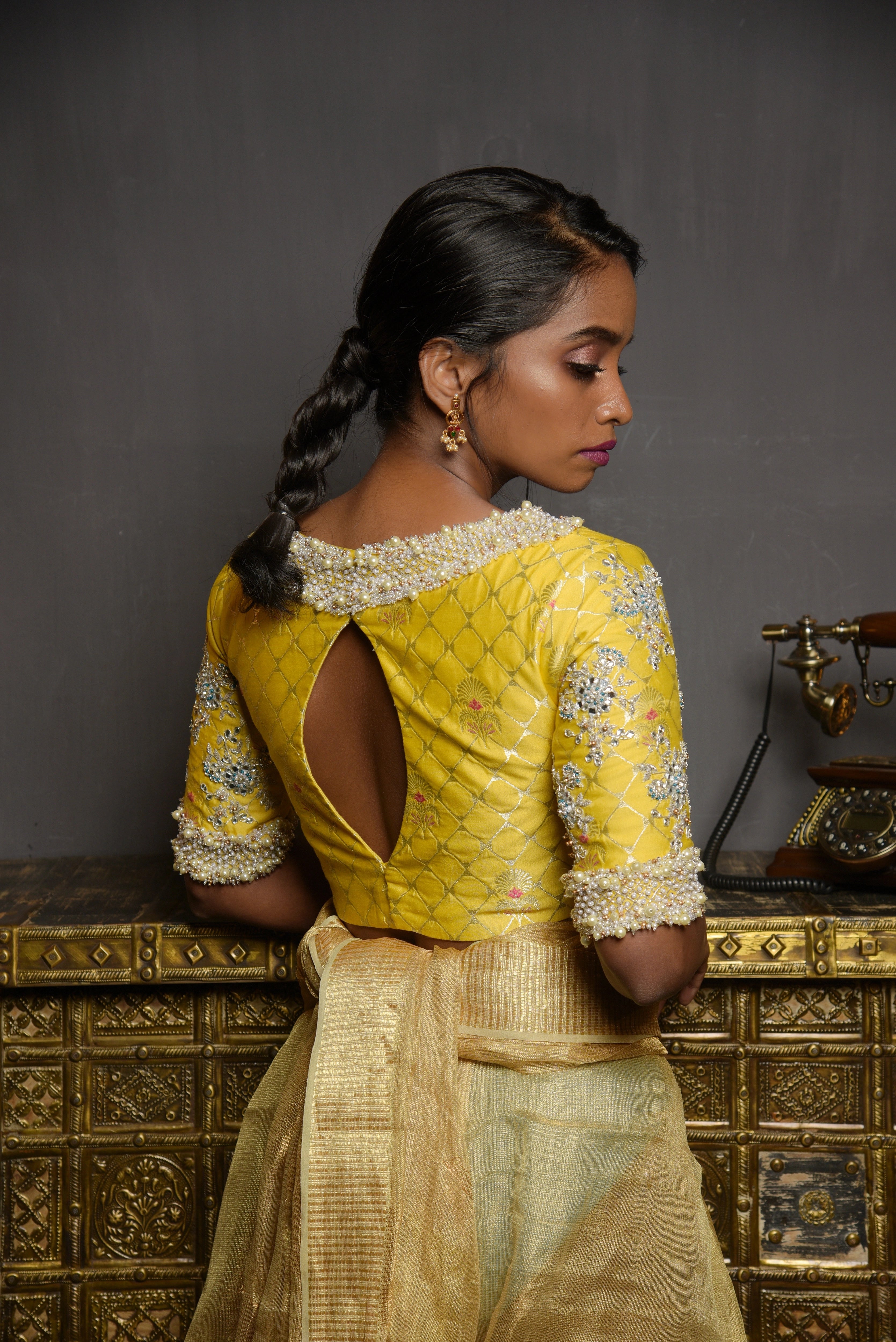 Model Pravallika Prasanna Raju posing for back blouse design in a yellow banarasi silk blouse with pearl embellishments on sleeves.
