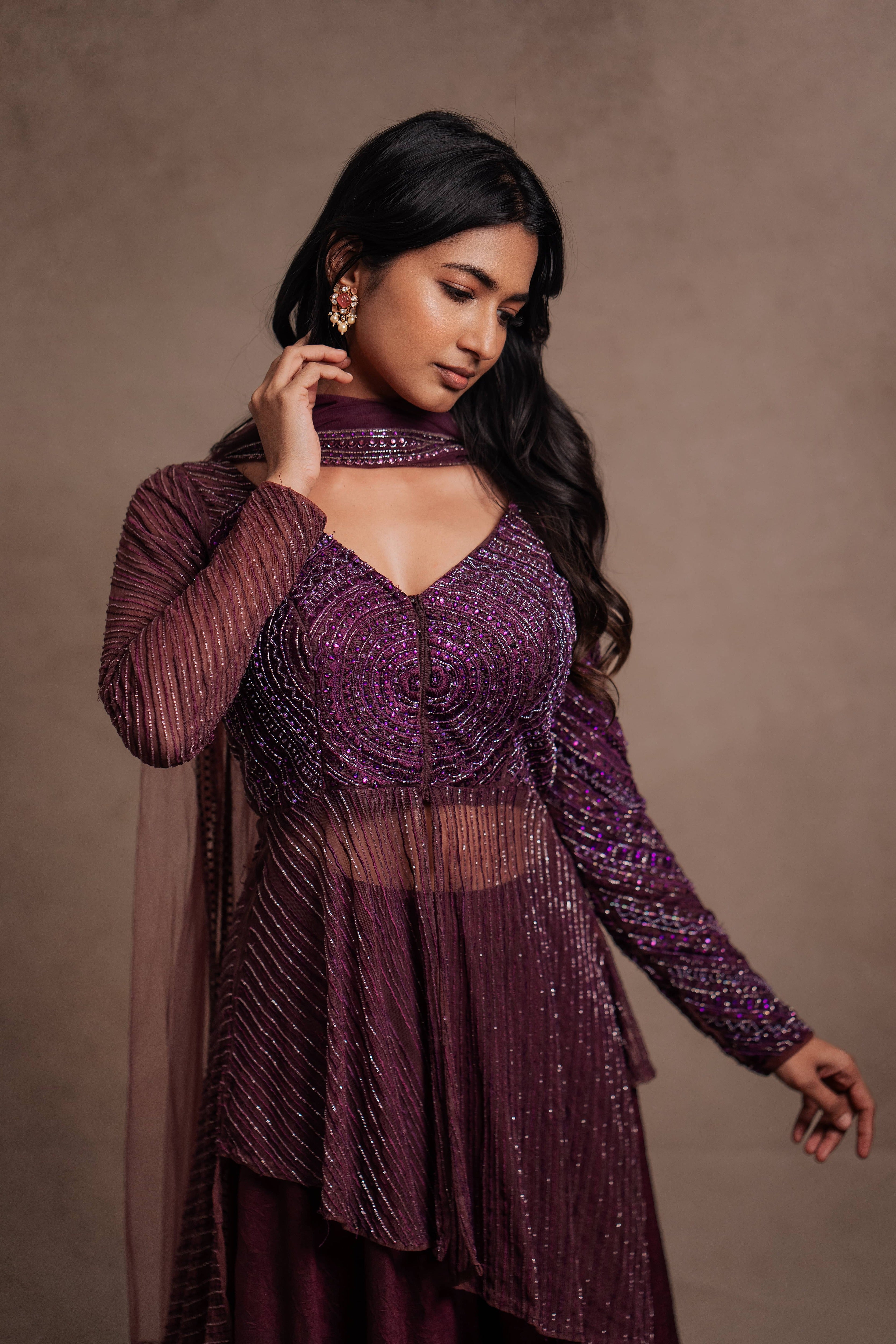 Model Premika Sekar in aubergine peplum sharara posing with hand in hair