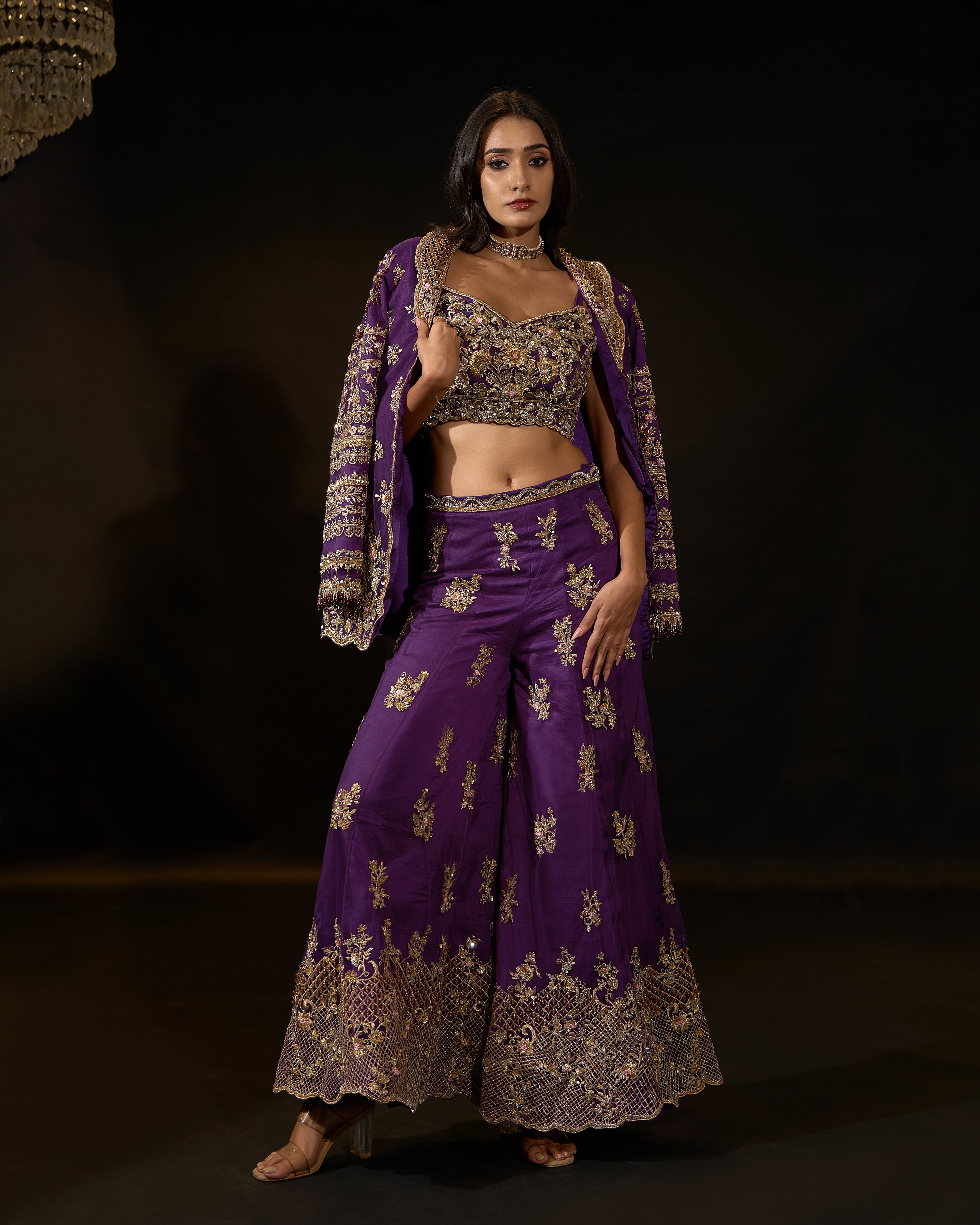 Model Rheyea in a purple jacket dress with bralette and palazzo pants. jacket over shoulder and one hand on thigh.