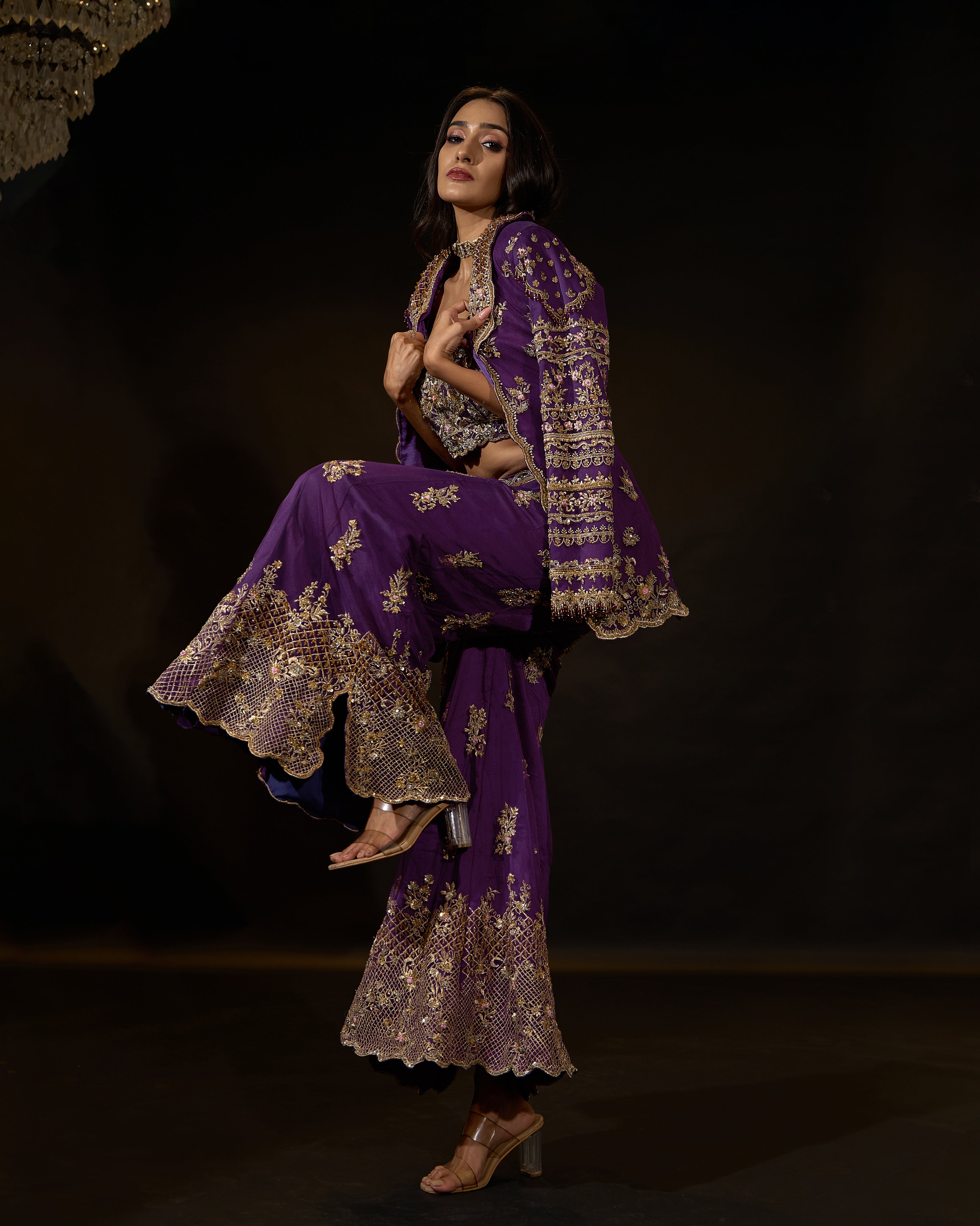 Model Rheyea in a purple jacket dress with bralette and palazzo pants. side profile with one leg up pose.