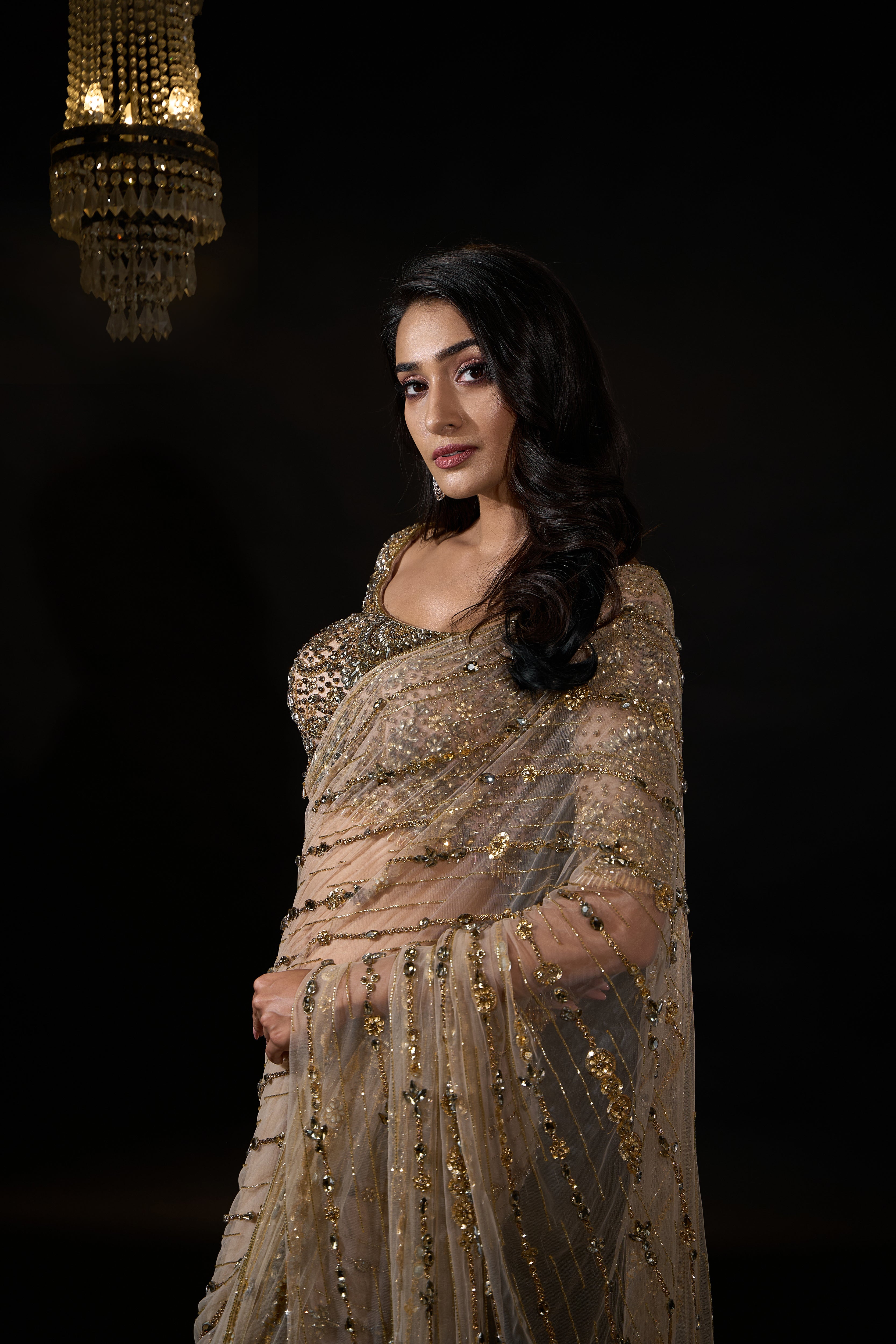 Model Rheyea in signature golden beige handcrafted net saree paired with a heavily embellished blouse by Archana Karthick. Stone work all over cups of blouse and hand over waist.
