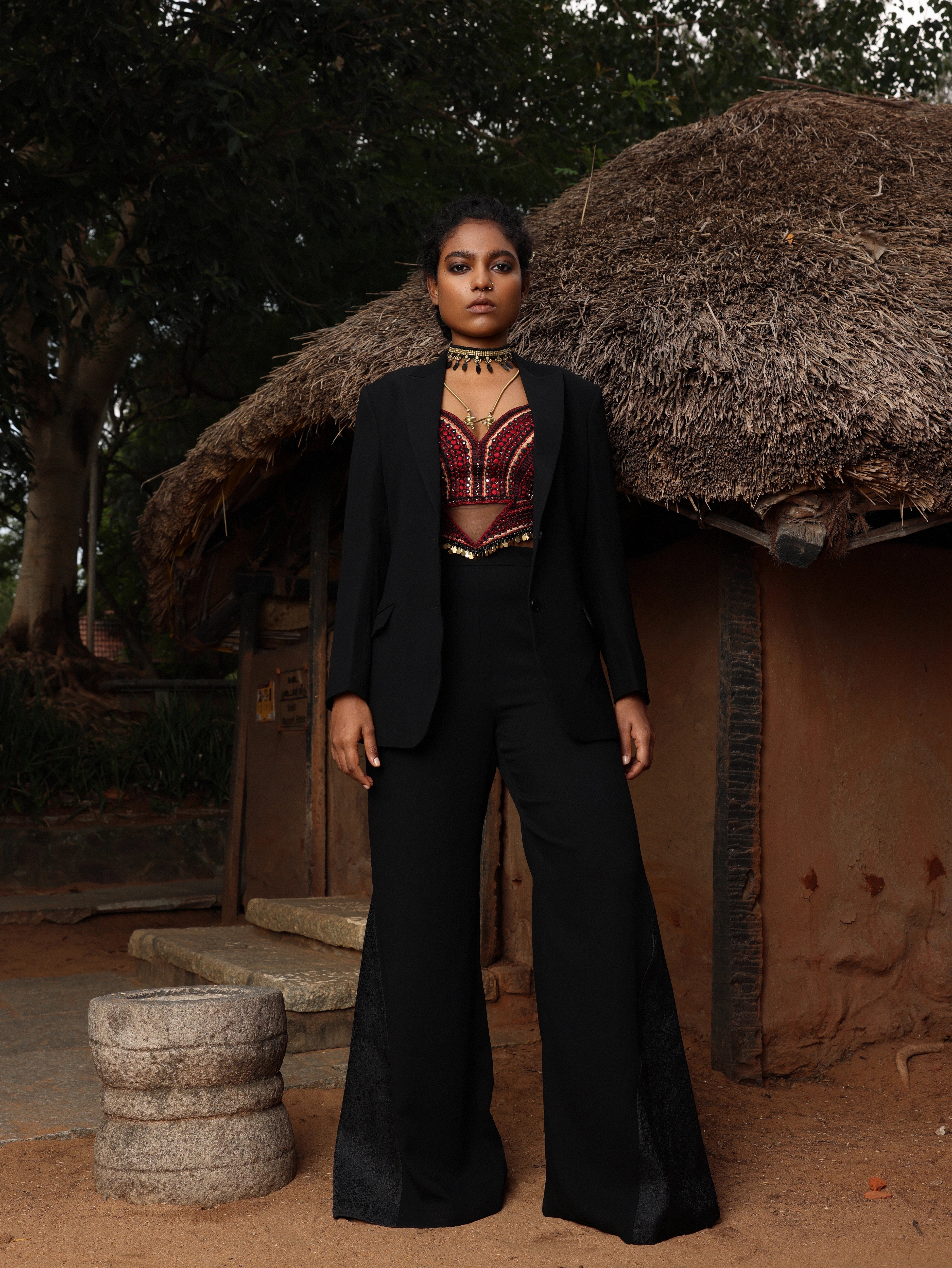 Model in black pantsuit with handcrafted corset. Posing outside a hut.