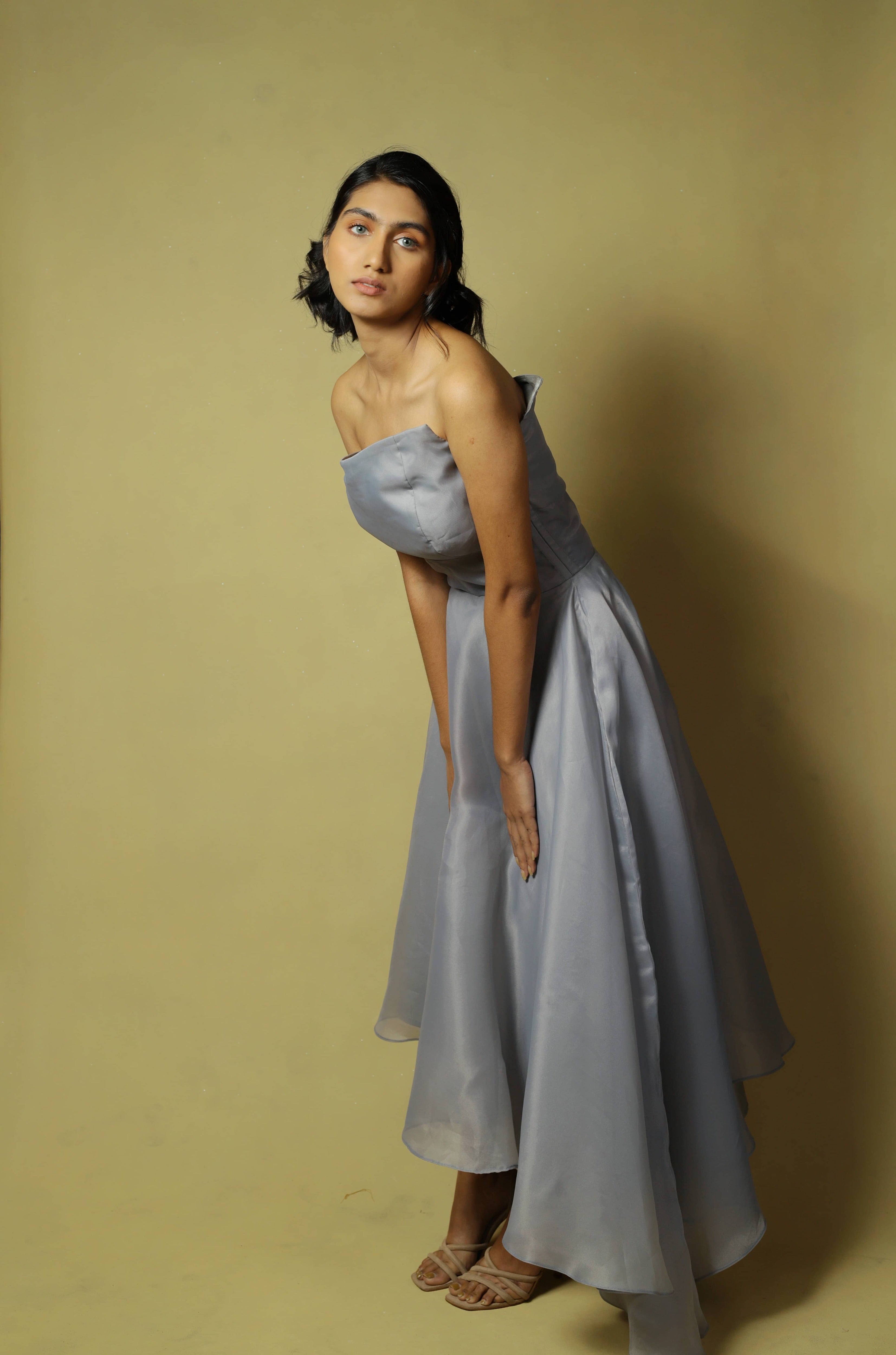 Model posing bent forward and looking to her left in a silver organza dress designed by Archana Karthick.