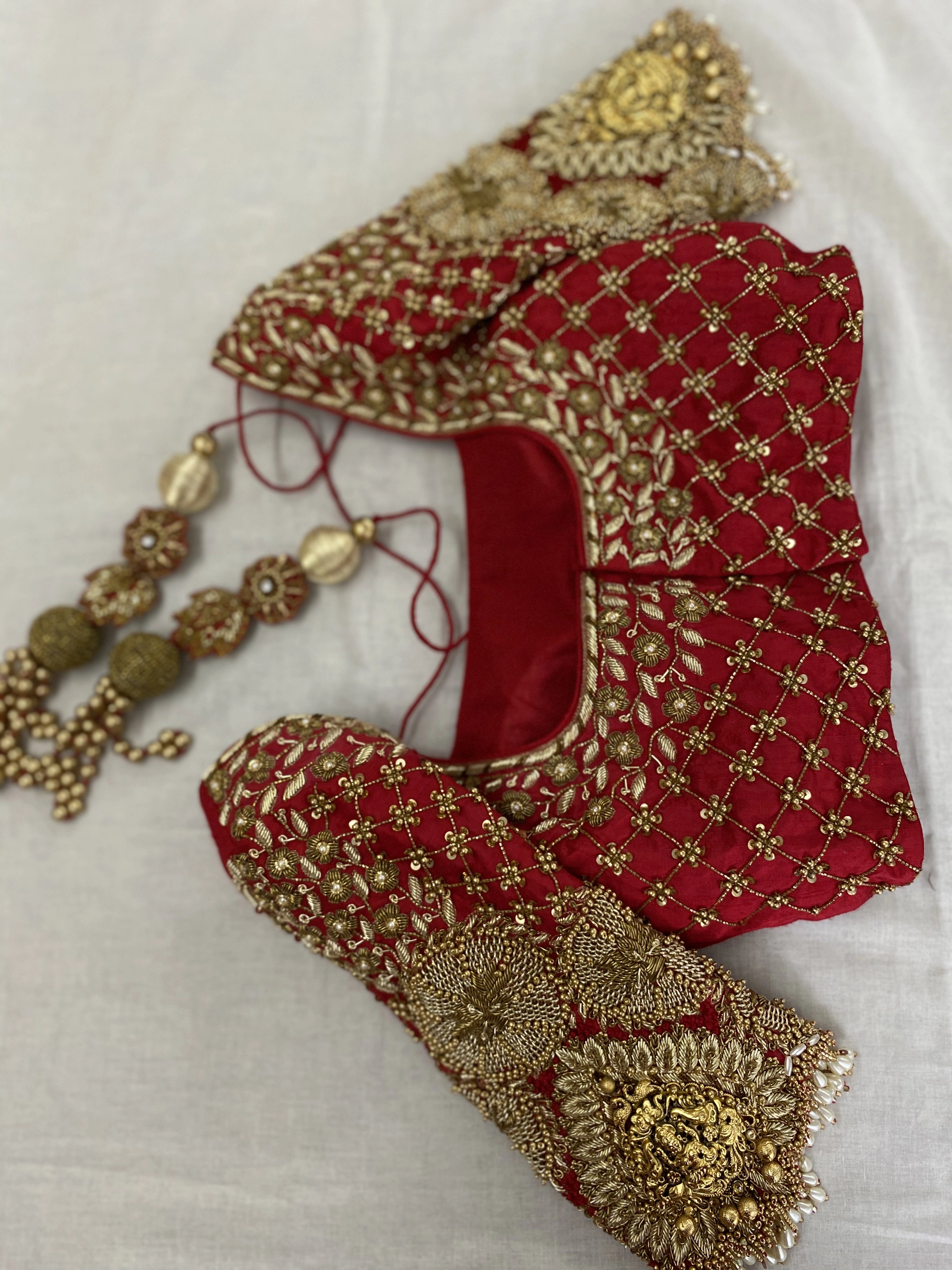 Photo of a handcrafted bridal red raw silk blouse embellished with zardozi, pearls, beads with goddess pendants on sleeves designed by Archana Karthick.