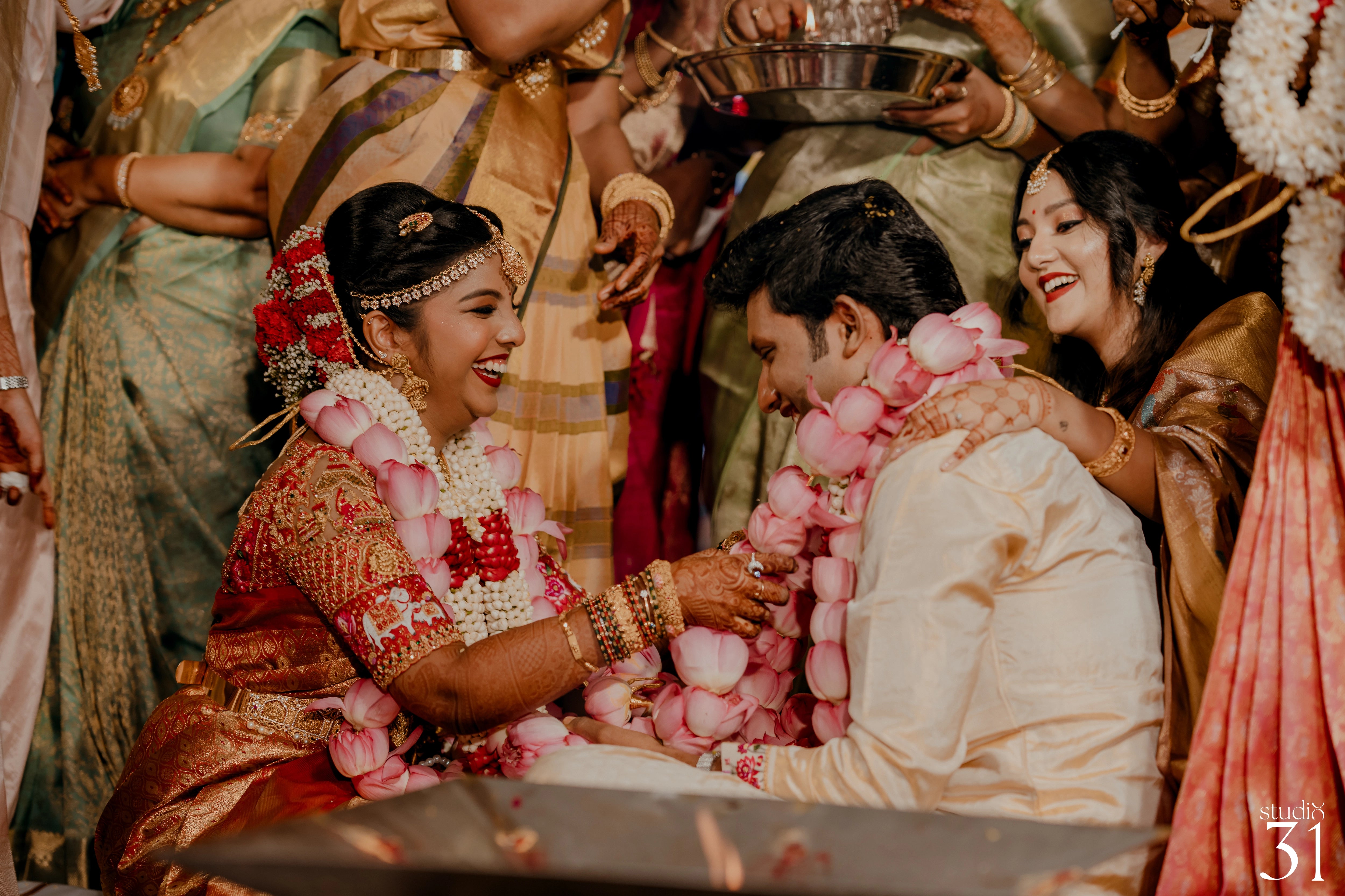 Pooja & Rhevanth smiiling for photos for their wedding in red silk blouse and white silk veshti and shirt - intricately handcrafted by team Archana Karthick.