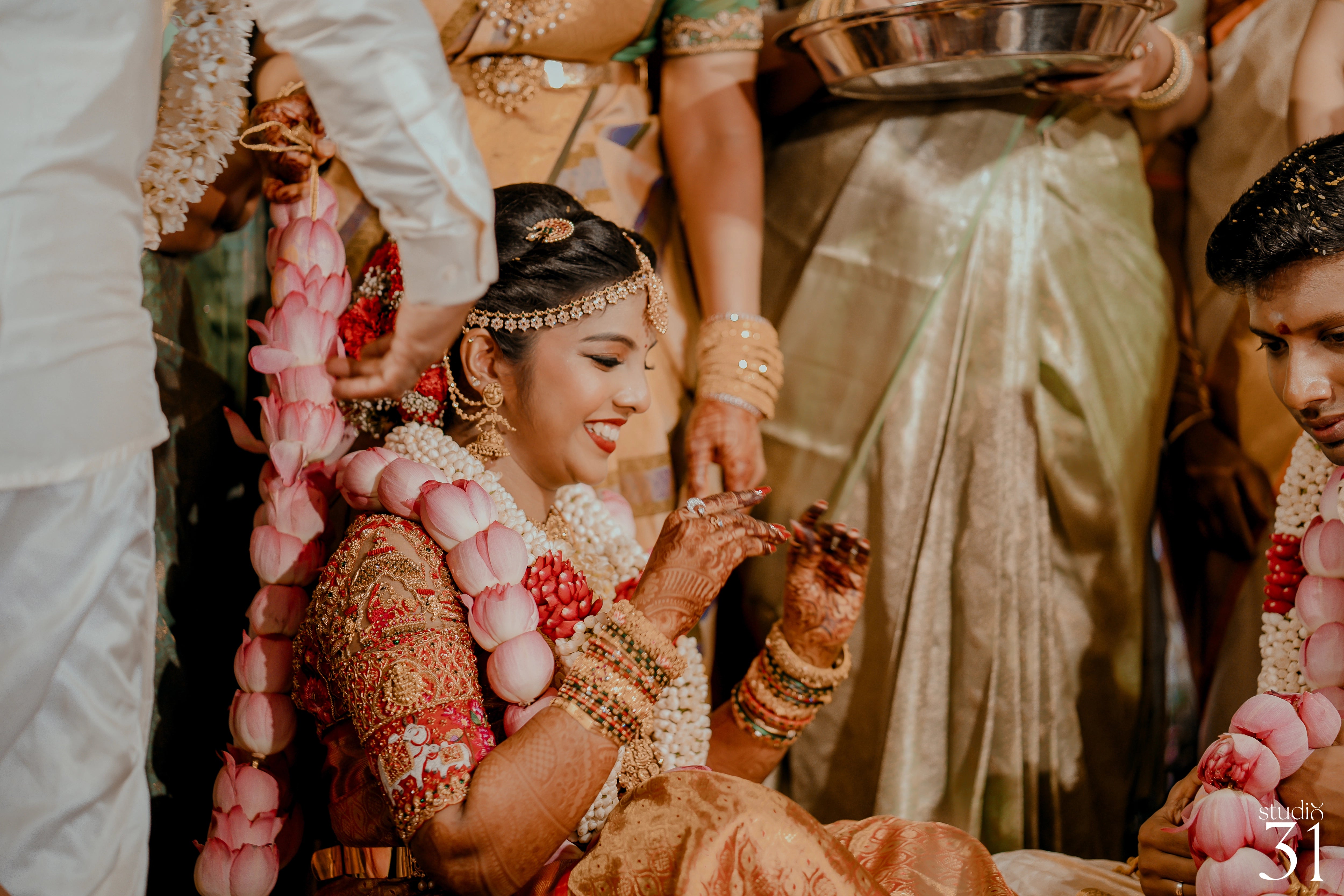 Pooja & Rhevanth smiiling for photoshoot for their wedding in red silk blouse and white silk veshti and shirt - intricately handcrafted by team Archana Karthick.