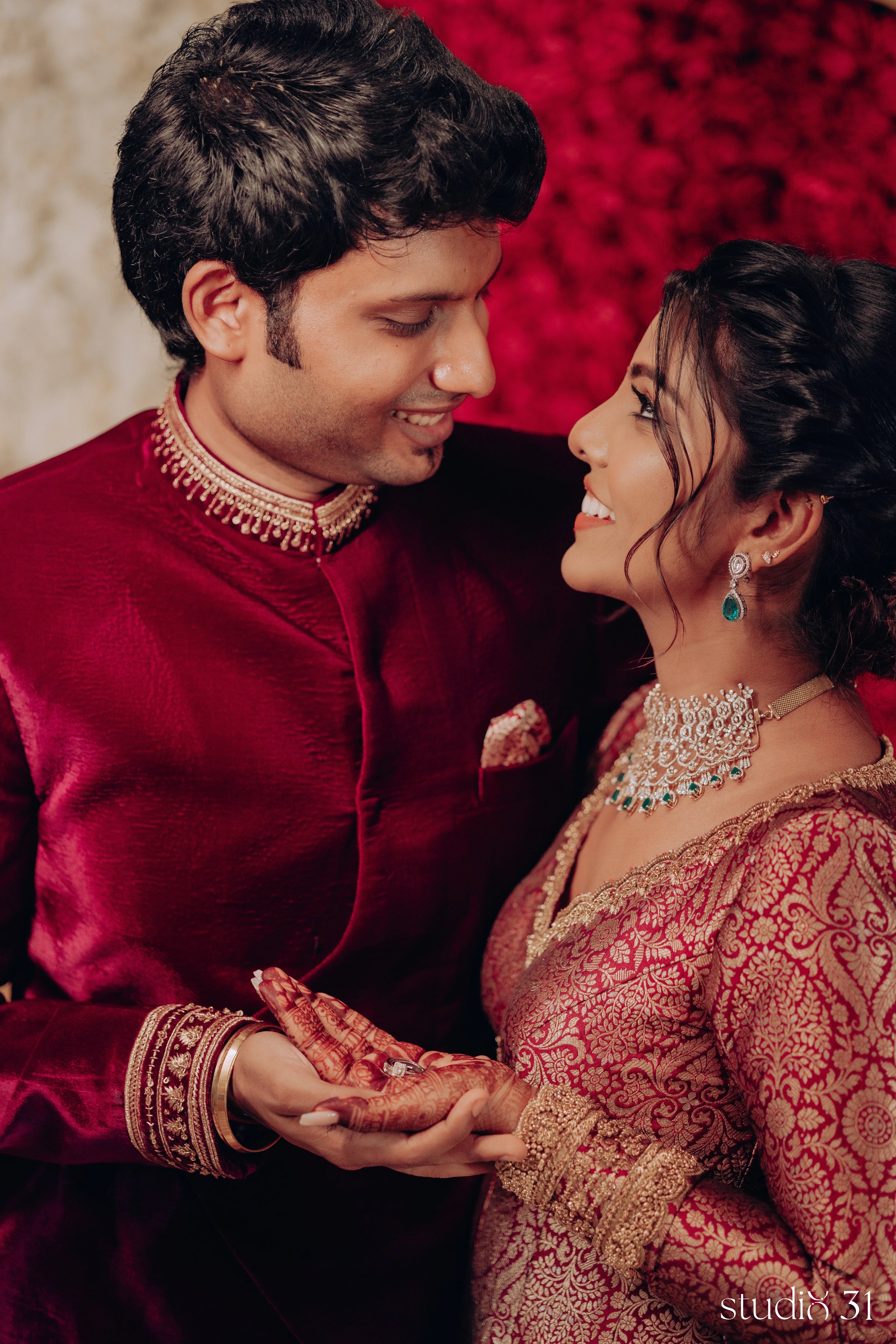 Pooja & Rhevanth smiling during their engagement in a maroon ensemble by Archana Karthick