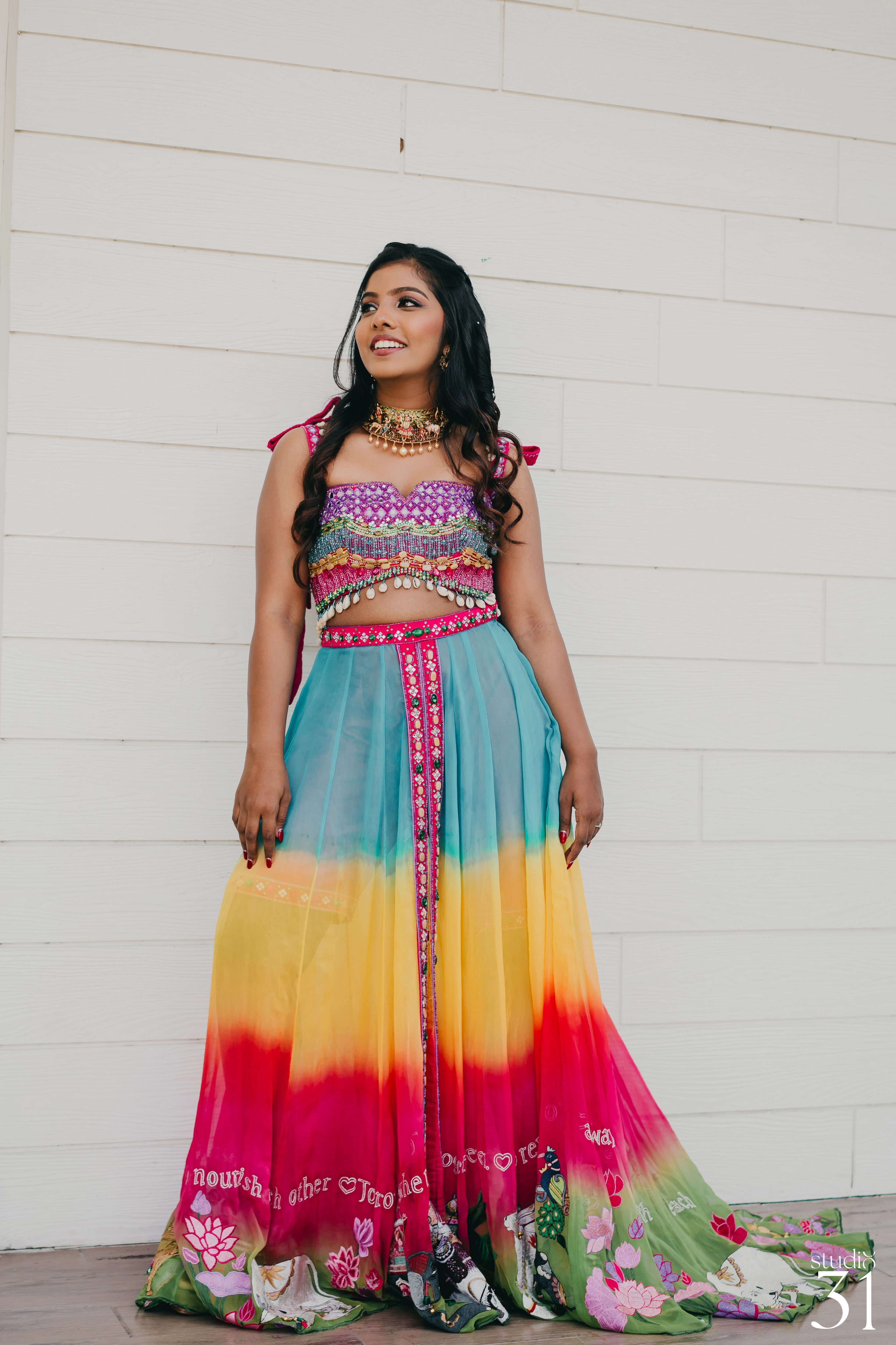 Pooja smiling in a multi-colored fusion lehenga for her mehendi, dyed and intricately handcrafted by team Archana Karthick.