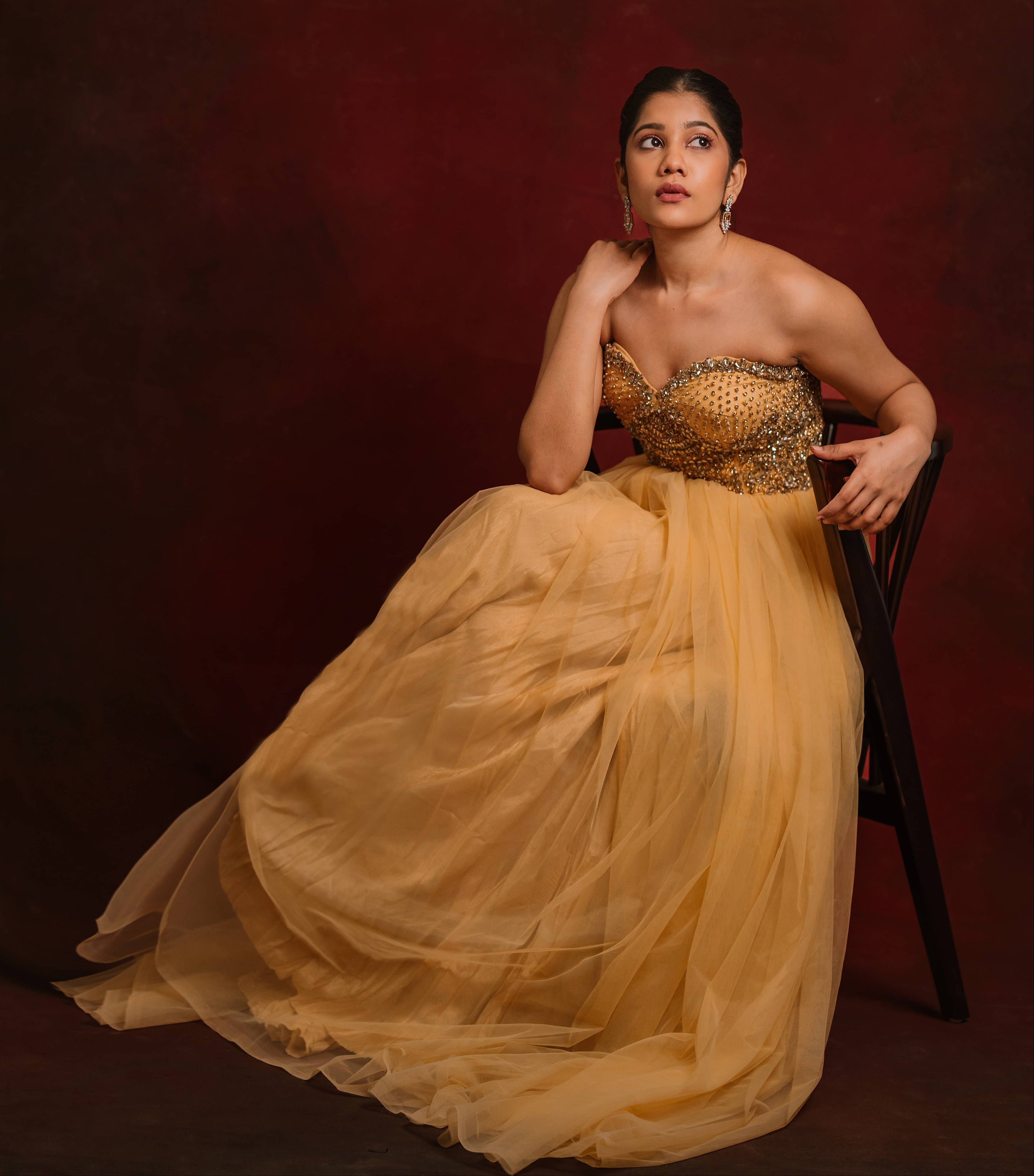 Posing seated in a gold corset dress intricately handcrafted with stones and sequins designed by team Archana Karthick.