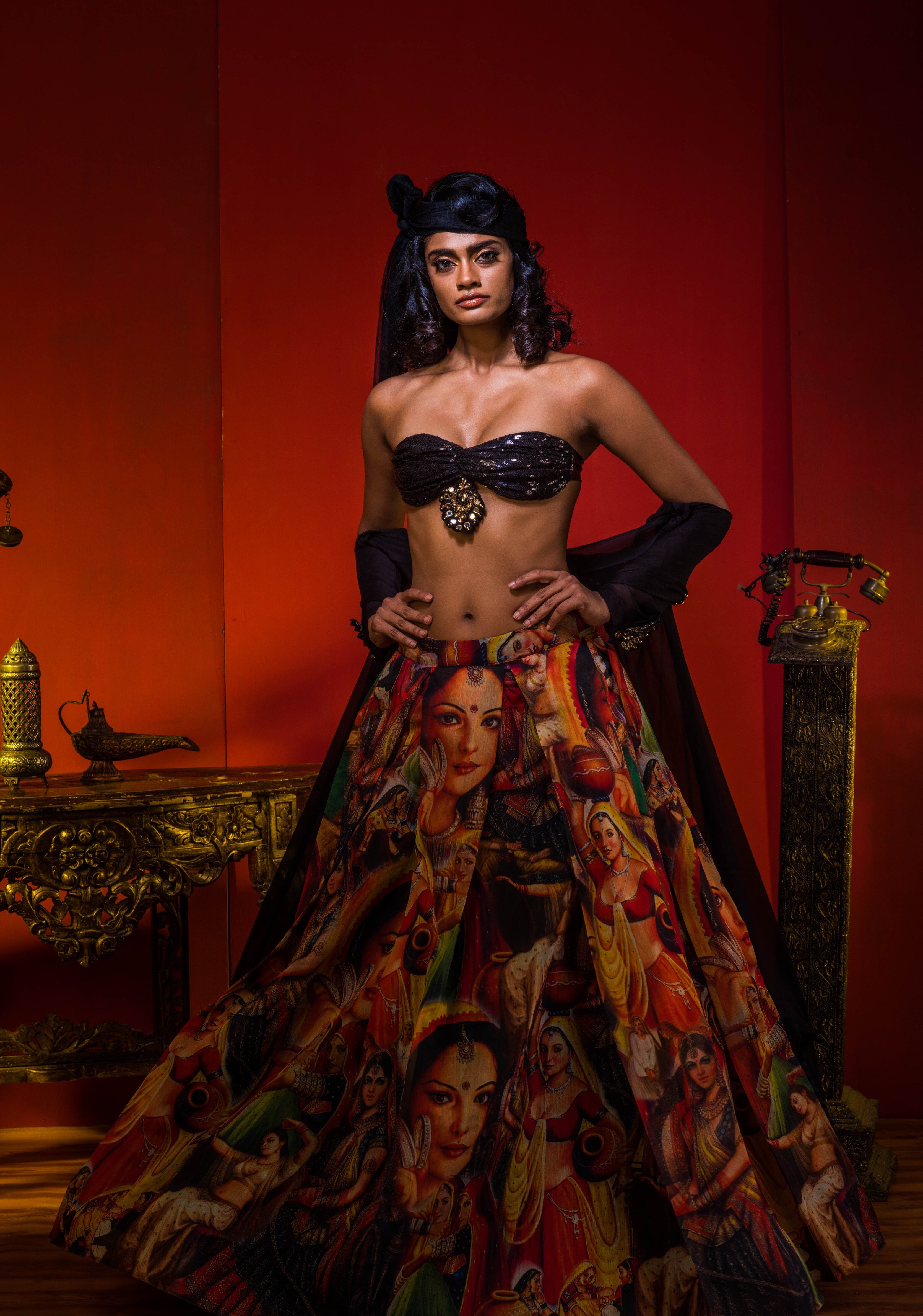 Supermodel Archana Akil Kumar in a heavily embellished black georgette bralette and long shrug paired with a printed colorful skirt looking staright into the lens with the shrug pulled down to her waist revealing the bralette and enhancing the fall of the shrug.