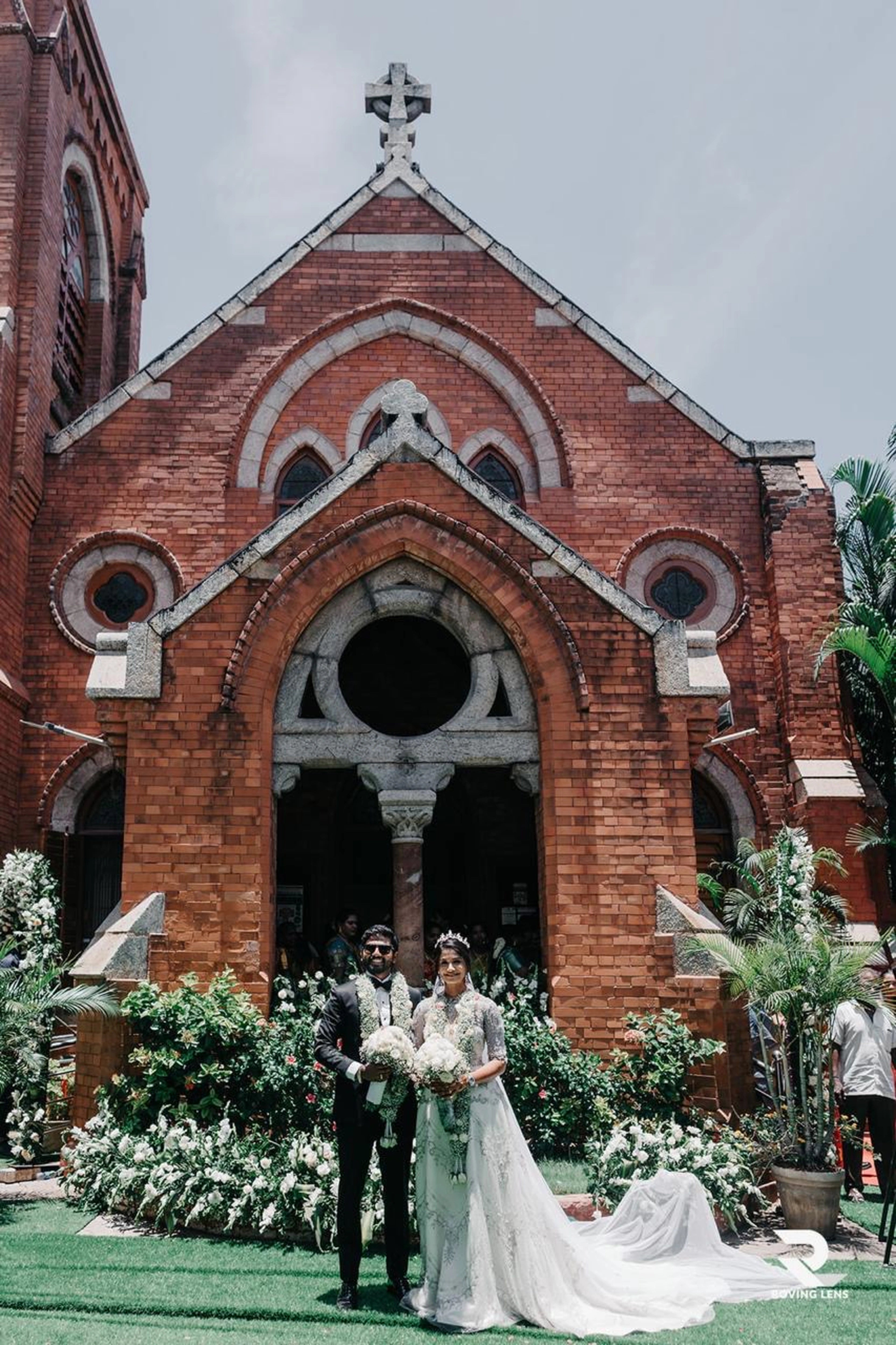 Wedding couple standing in front of a brick church with floral decorations.