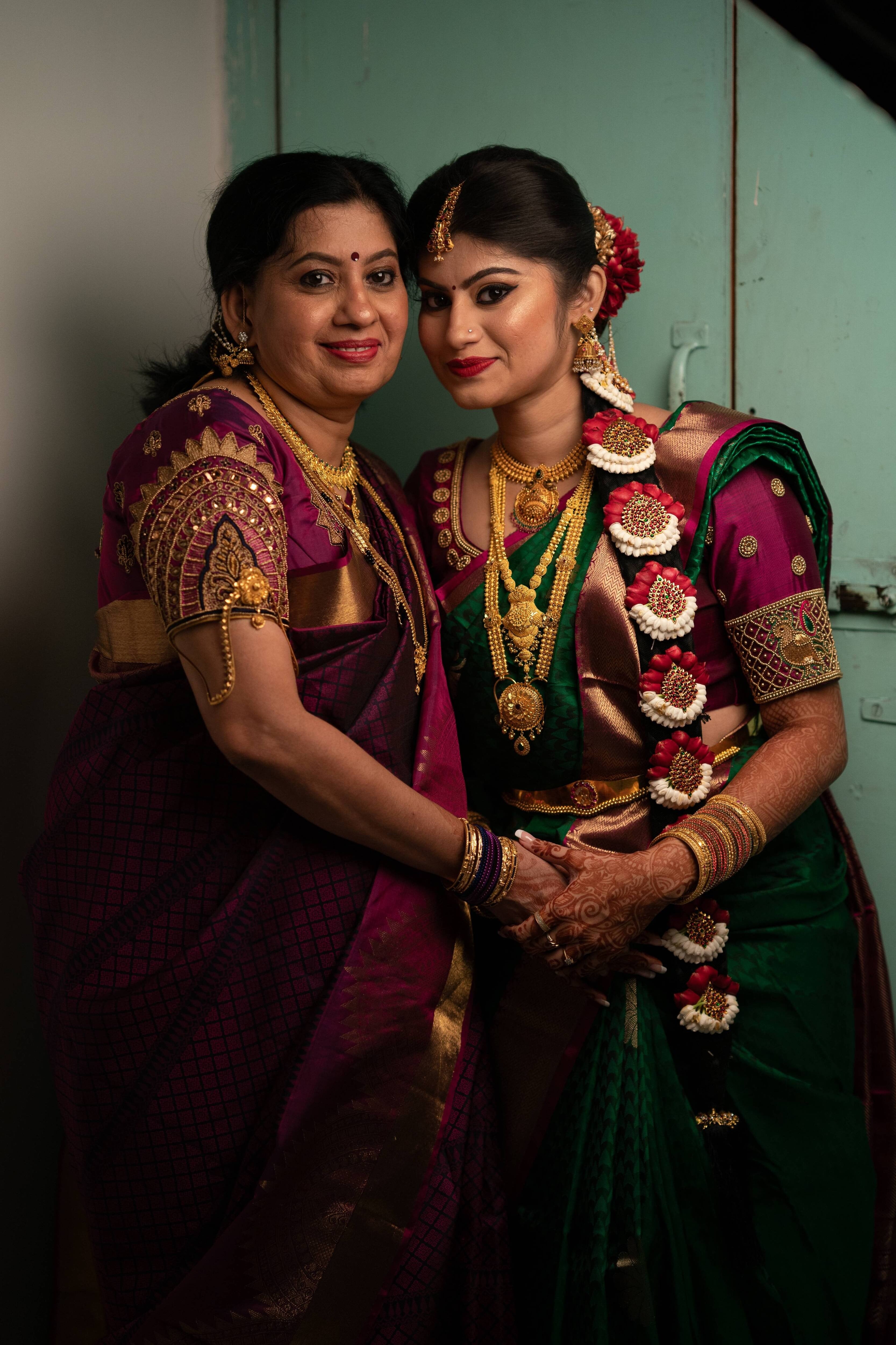 Bride Vandita and her mother are seen here in our silk aubergine colored blouse.This is designed for her engagement. Resham, zardozi, beads and mirror work techniques used on the blouse. The bride and her mother are holding each other's hand in an emotional mother-daughter pose.