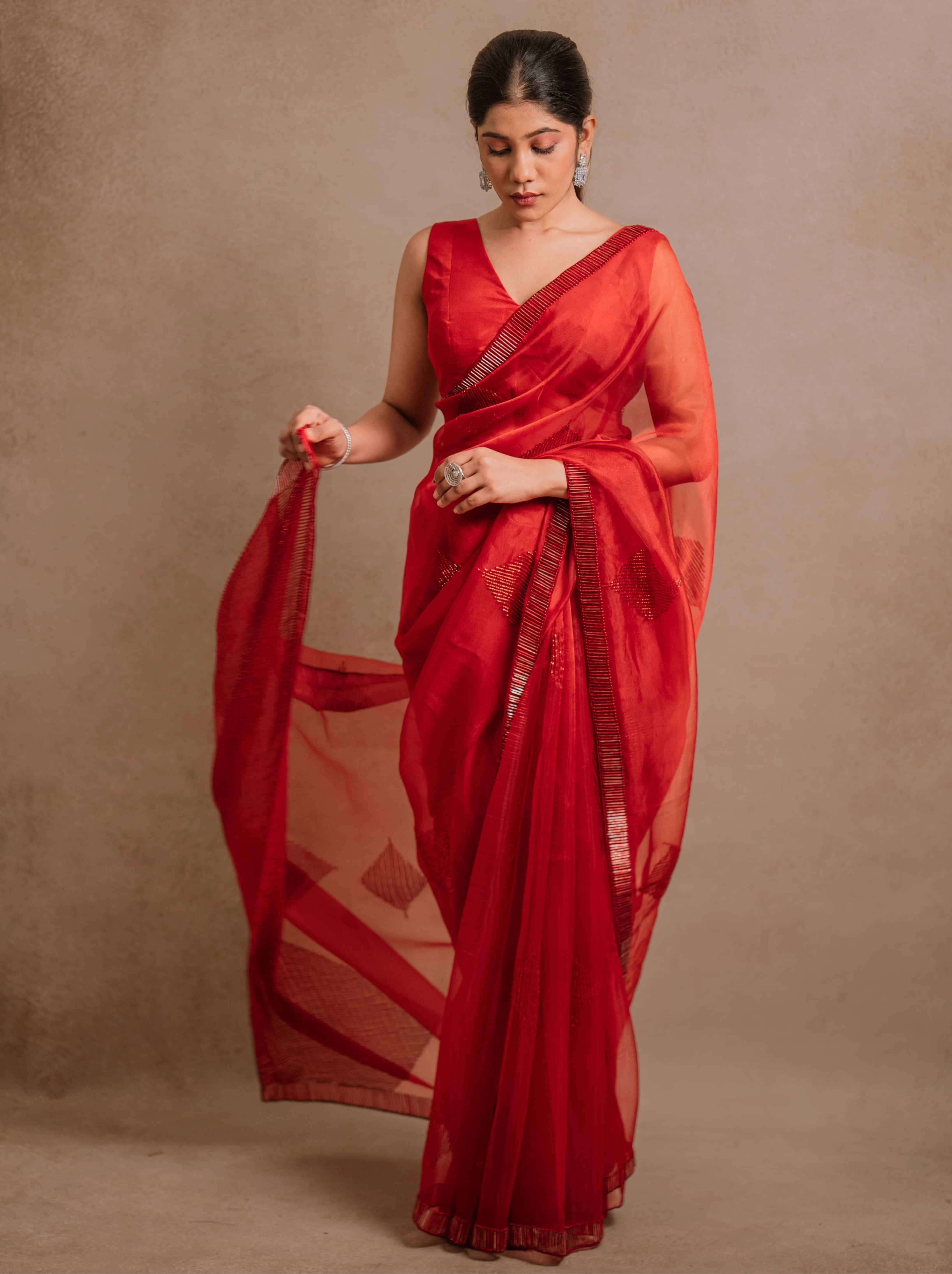 looking down in a red-orange organza saree intricately handcrafted with cutdana lines, designed by team Archana Karthick.