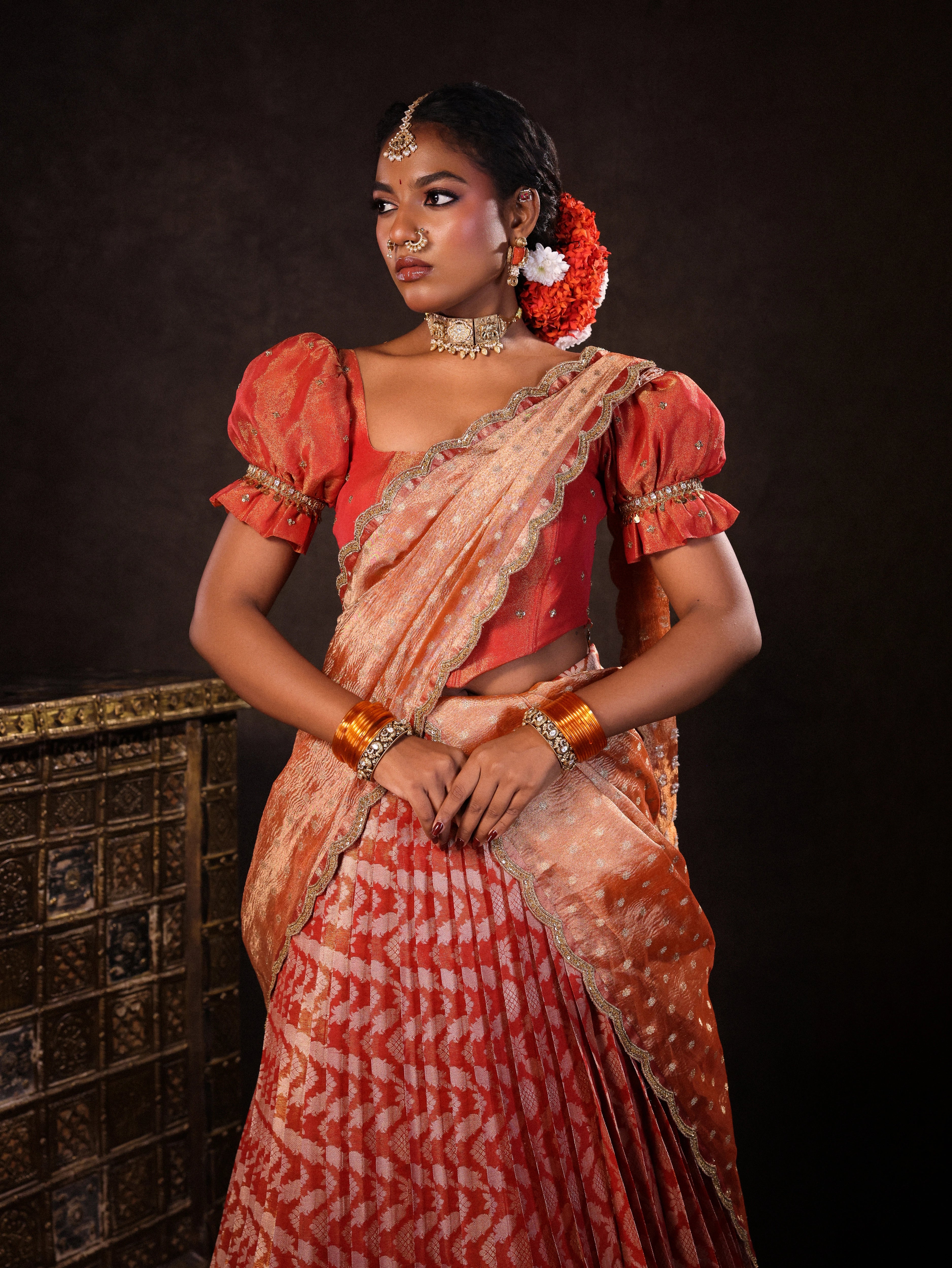 Model Ashika pose in orange jacquard silk half saree with glass bangles and jewellery from NAC