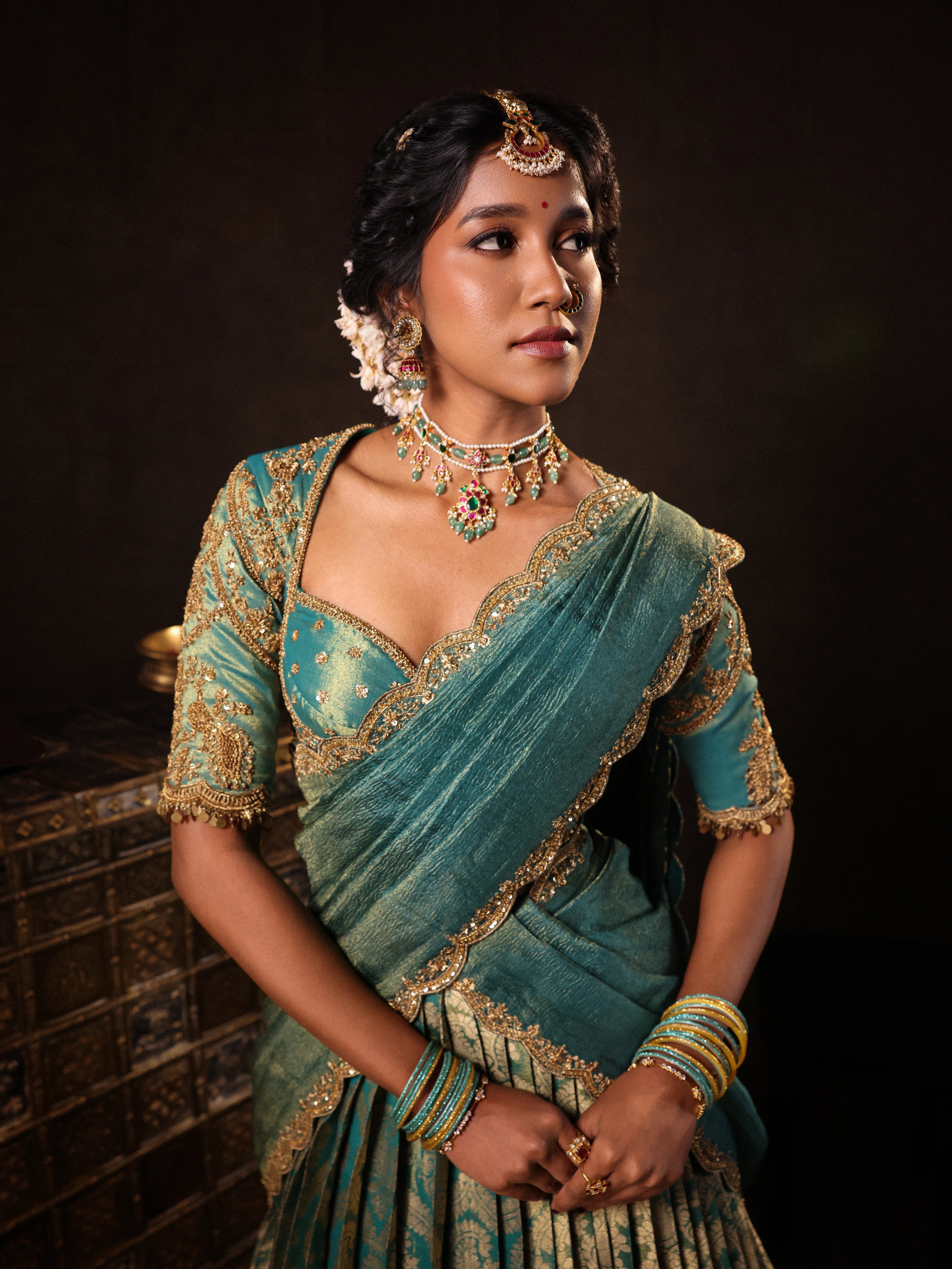 Model Gayathri Dhanasekar in a teal jacquard silk half saree with glass bangles and NAC jewellery.