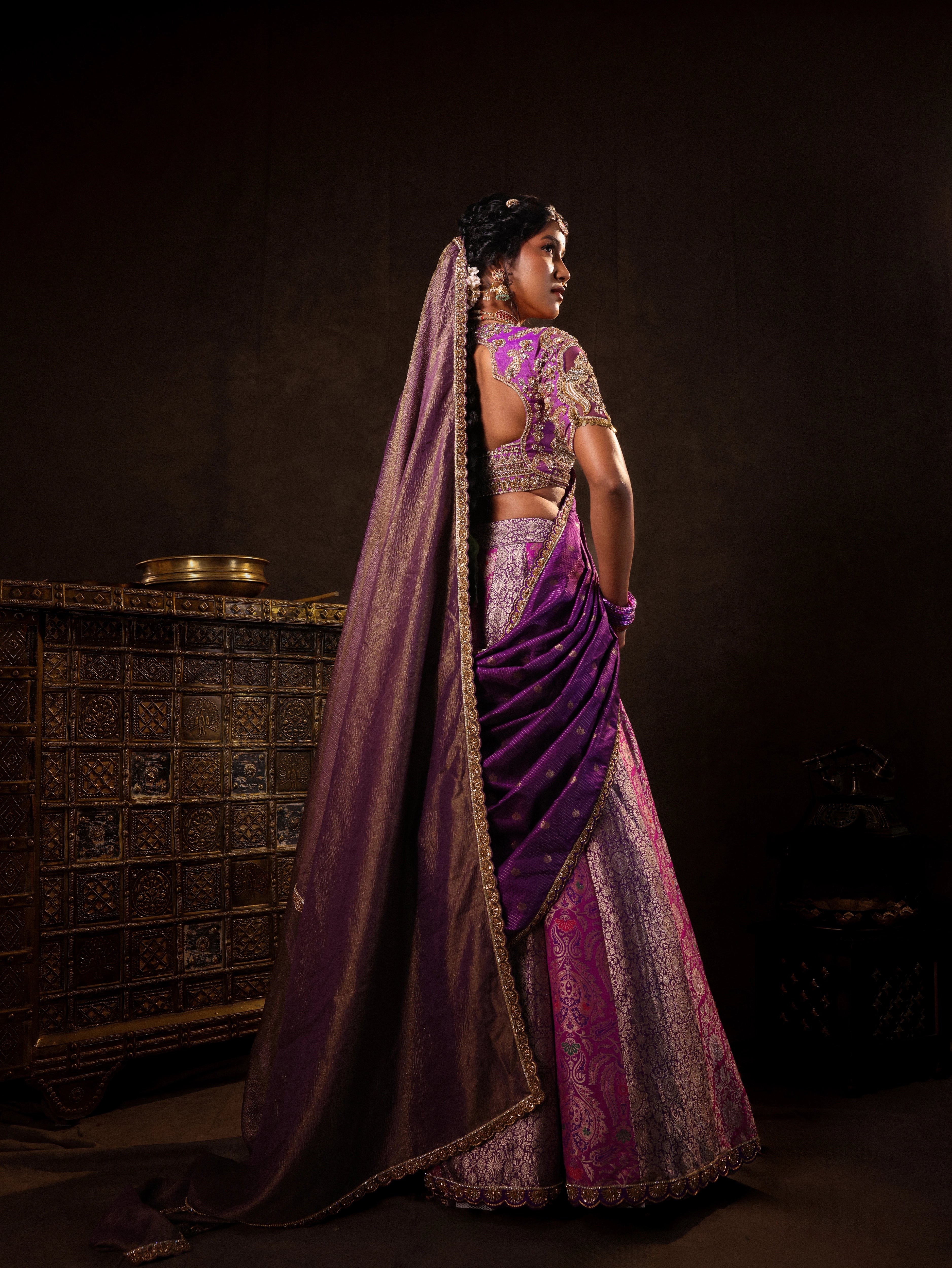 Model Gayathri Dhanasekar pose in a purple banarasi brocade silk half saree with glass bangles and NAC jewellery.