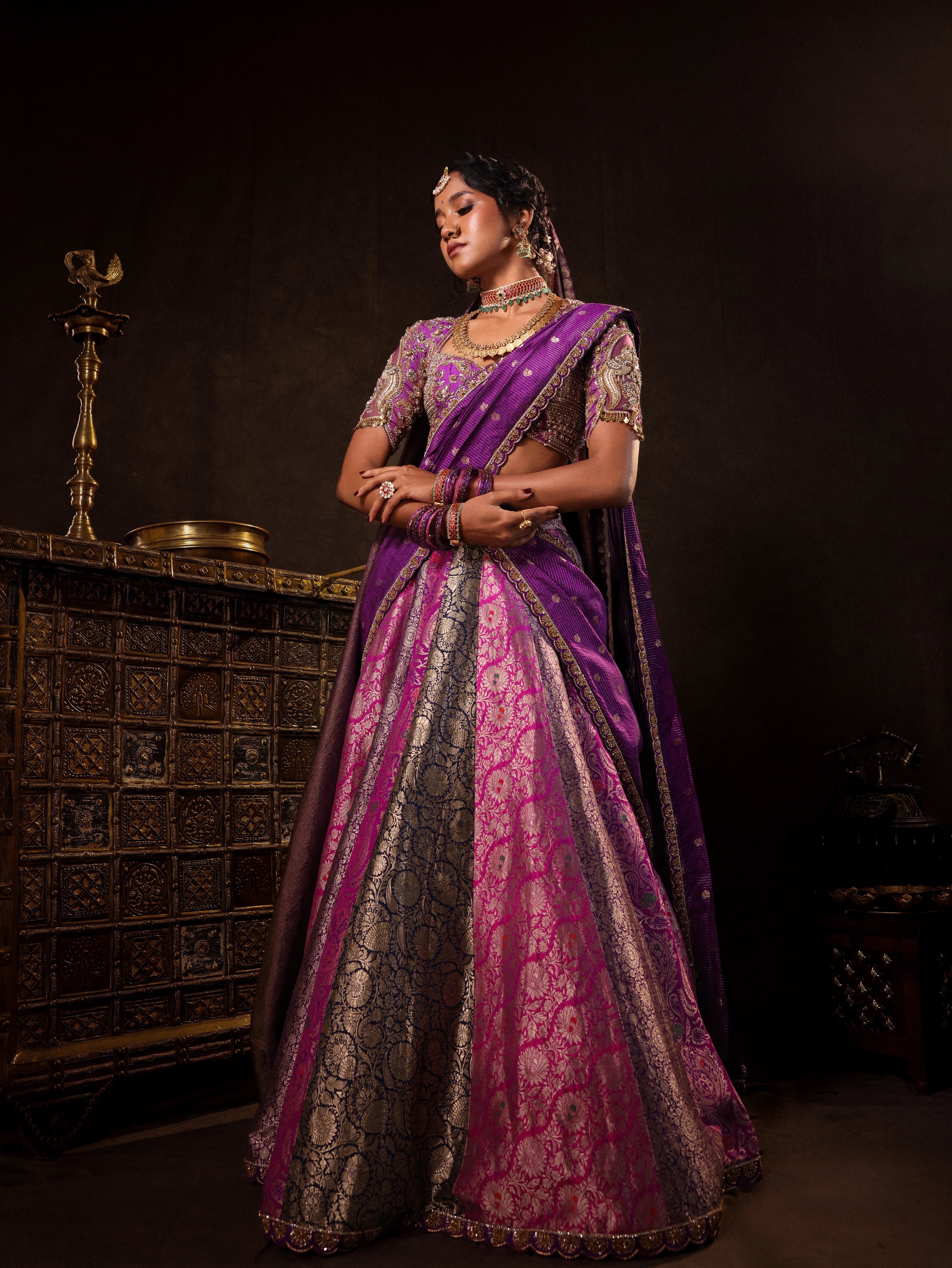 Model Gayathri Dhanasekar posing in a purple banarasi brocade silk half saree with glass bangles and NAC jewellery.
