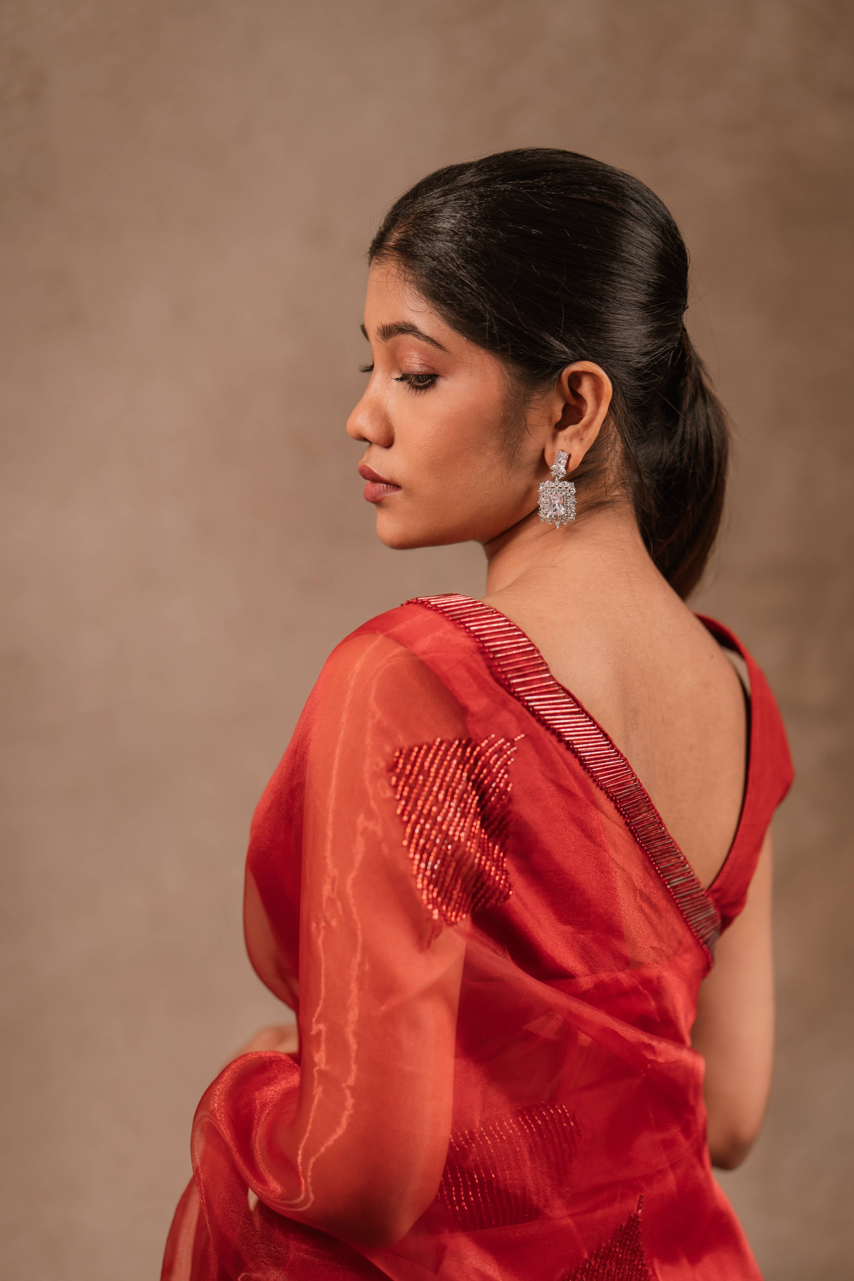 posing for back design in a red-orange organza saree intricately handcrafted with cutdana lines, designed by team Archana Karthick.