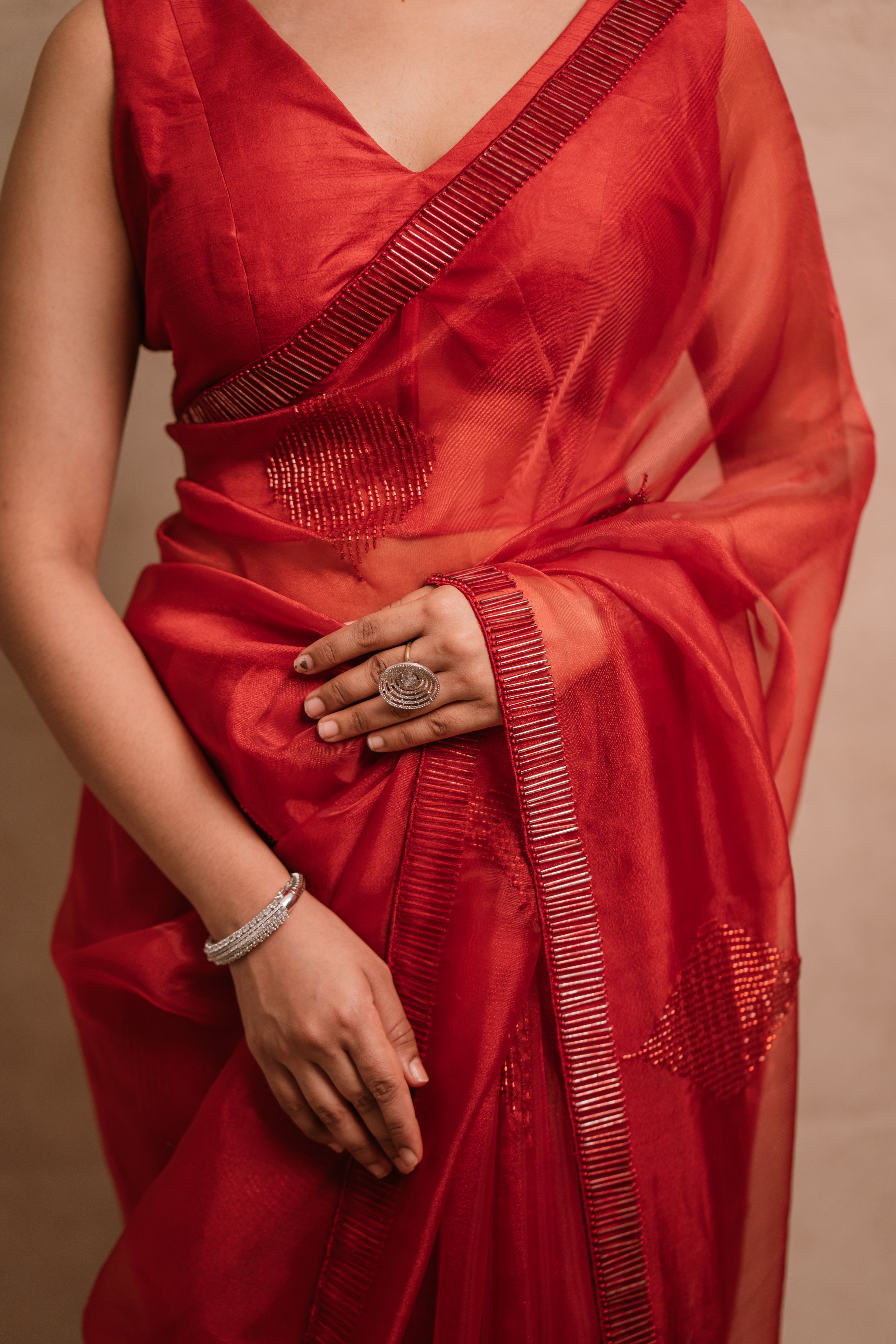 showcasing front in a red-orange organza saree intricately handcrafted with cutdana lines, designed by team Archana Karthick.