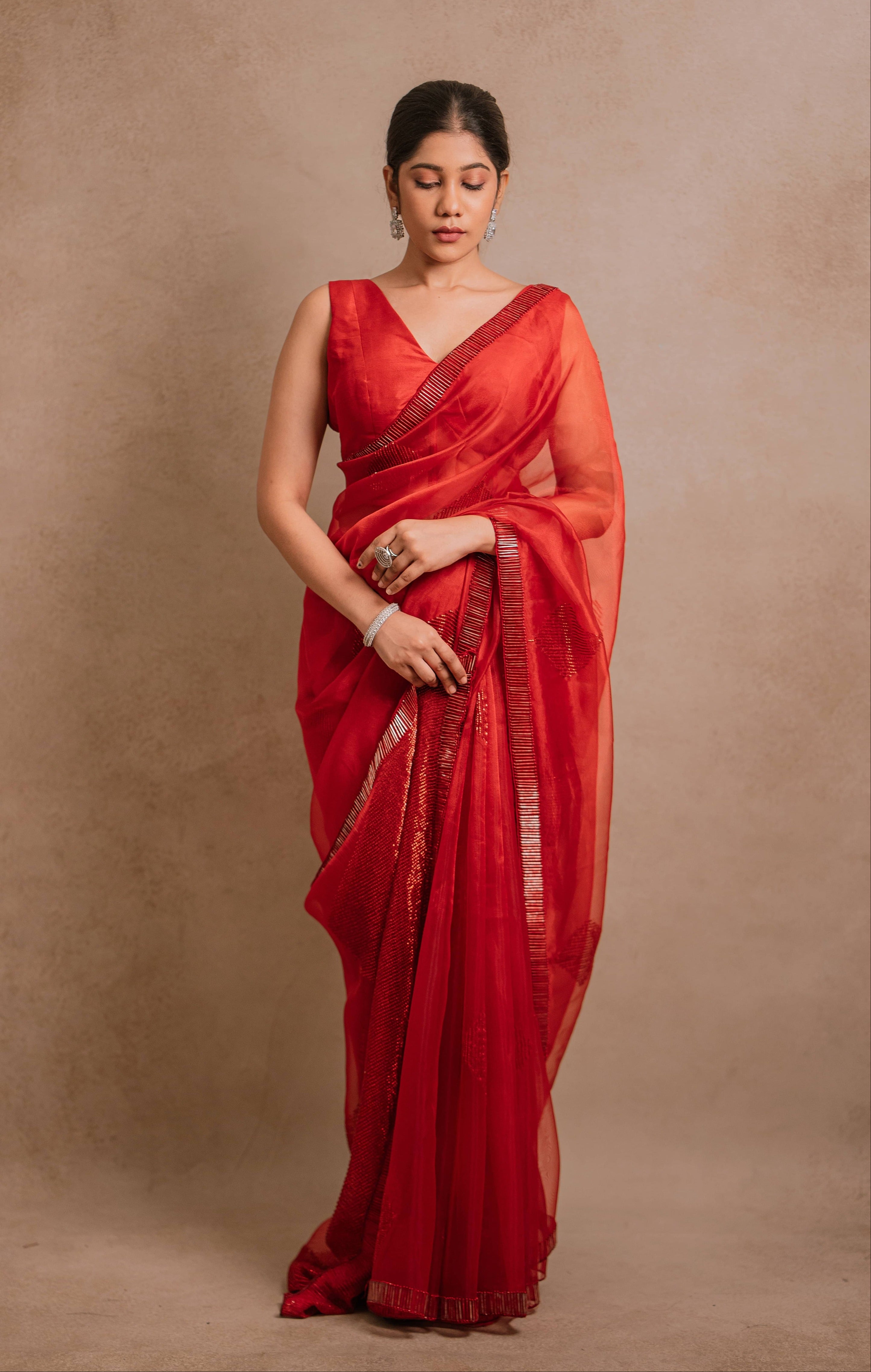 showcasing full front in a red-orange organza saree intricately handcrafted with cutdana lines, designed by team Archana Karthick.