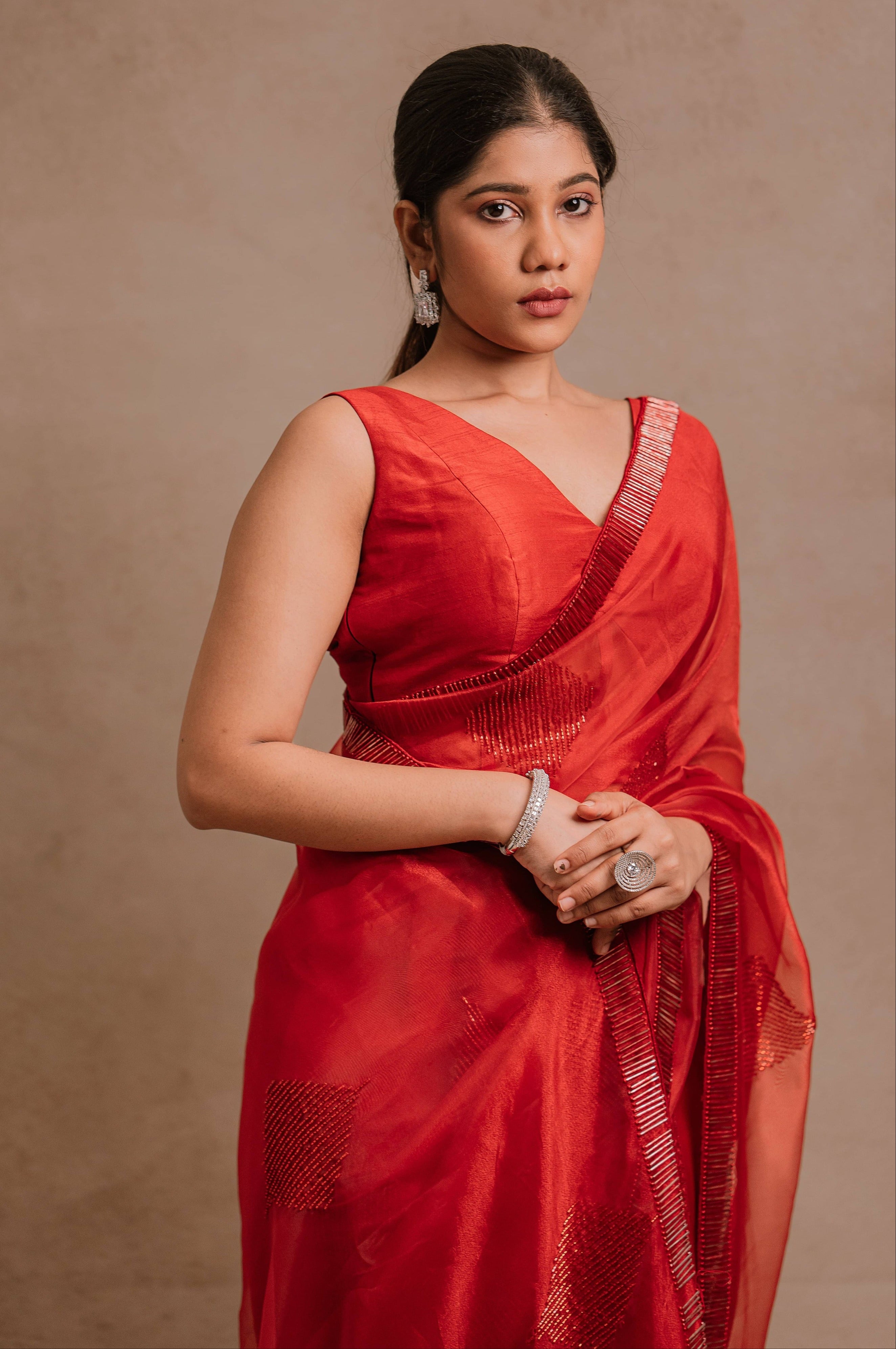 showcasing half front in a red-orange organza saree intricately handcrafted with cutdana lines, designed by team Archana Karthick.