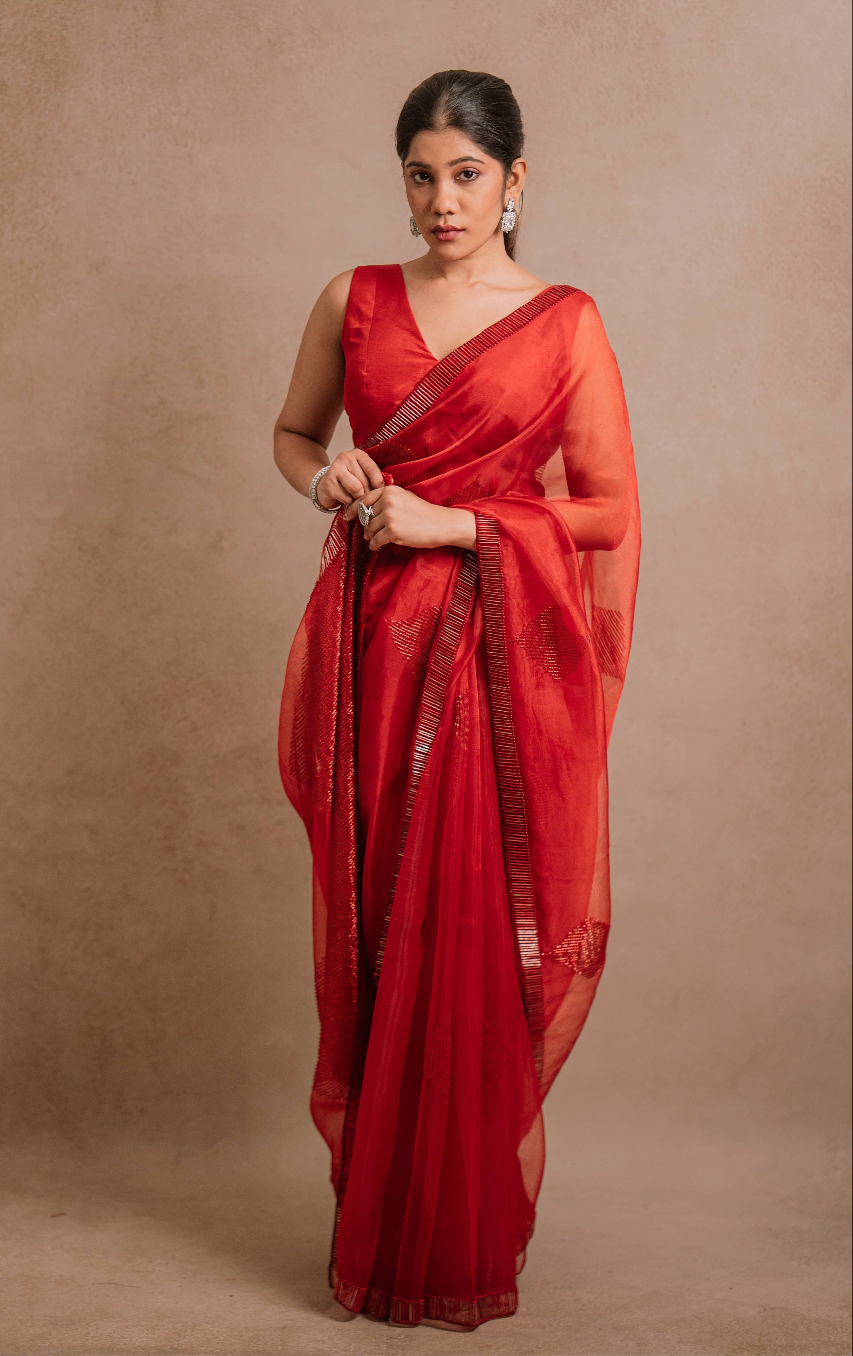 showcasing in a red-orange organza saree intricately handcrafted with cutdana lines, designed by team Archana Karthick.