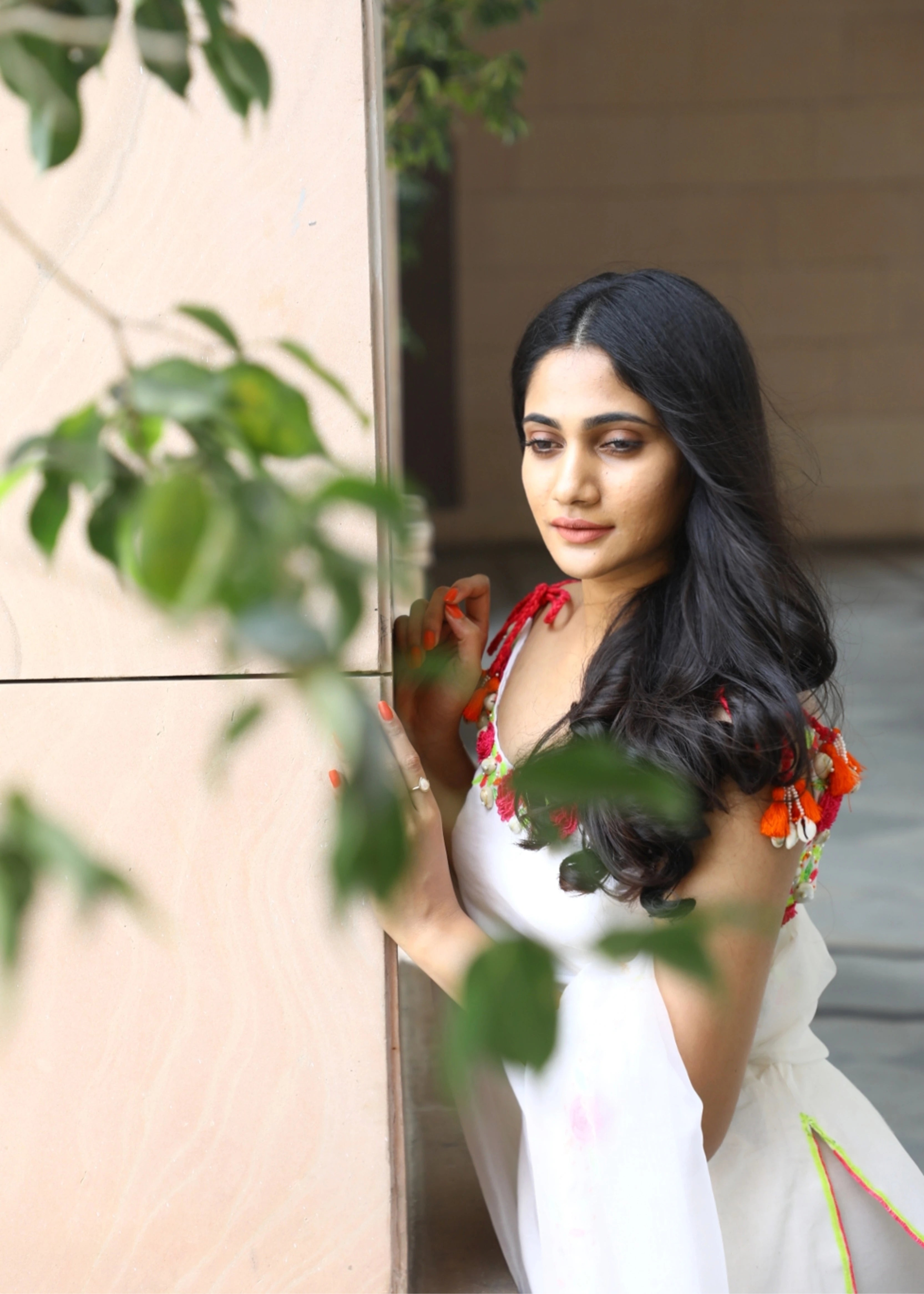 Actor and Influencer Losliya Mariyanesan leaning on wall in a gharara set handcrafted with handmade 3D Flowers, pom poms and sea shells. Designed by Archana Karthick