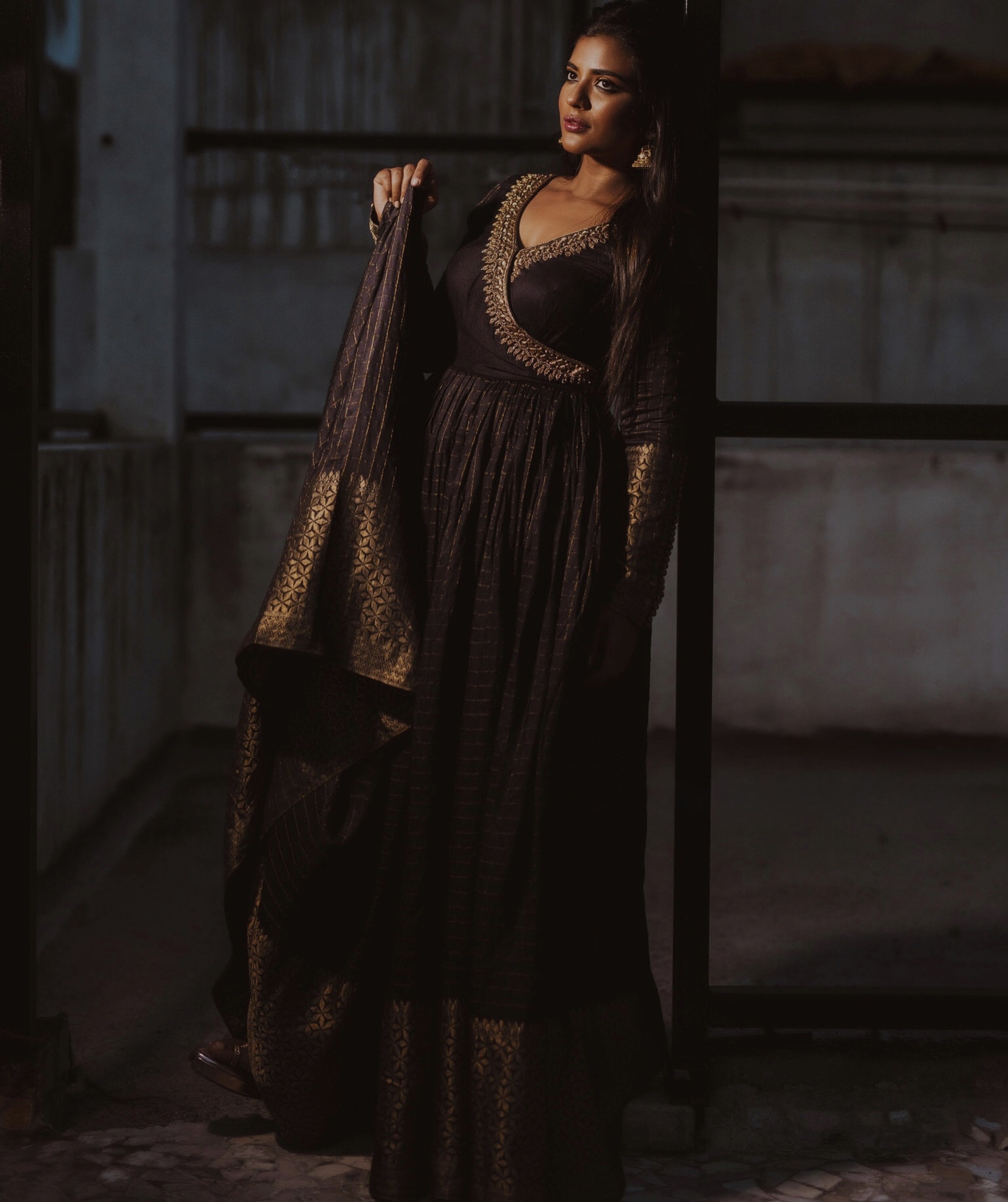 Actress Aishwarya Rajesh in a black silk angrakha anarkali looking away from camera with a smile and lifting the flare of the outfit
