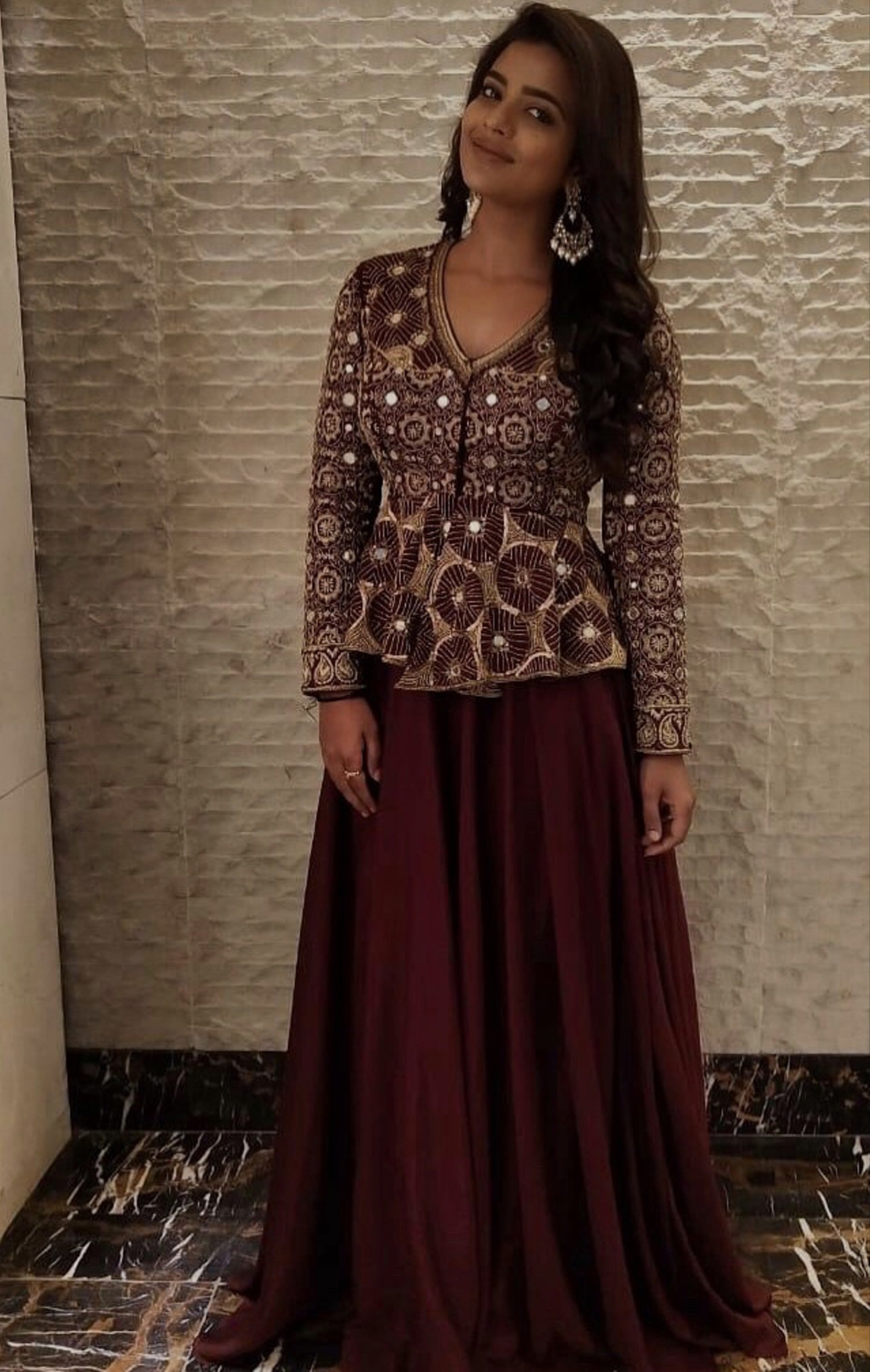 Actress Aishwarya Rajesh in a handcrafted peplum sharara in wine red for the promo of the movie world famous lover with vijay devarakonda. She is smiling at the camera