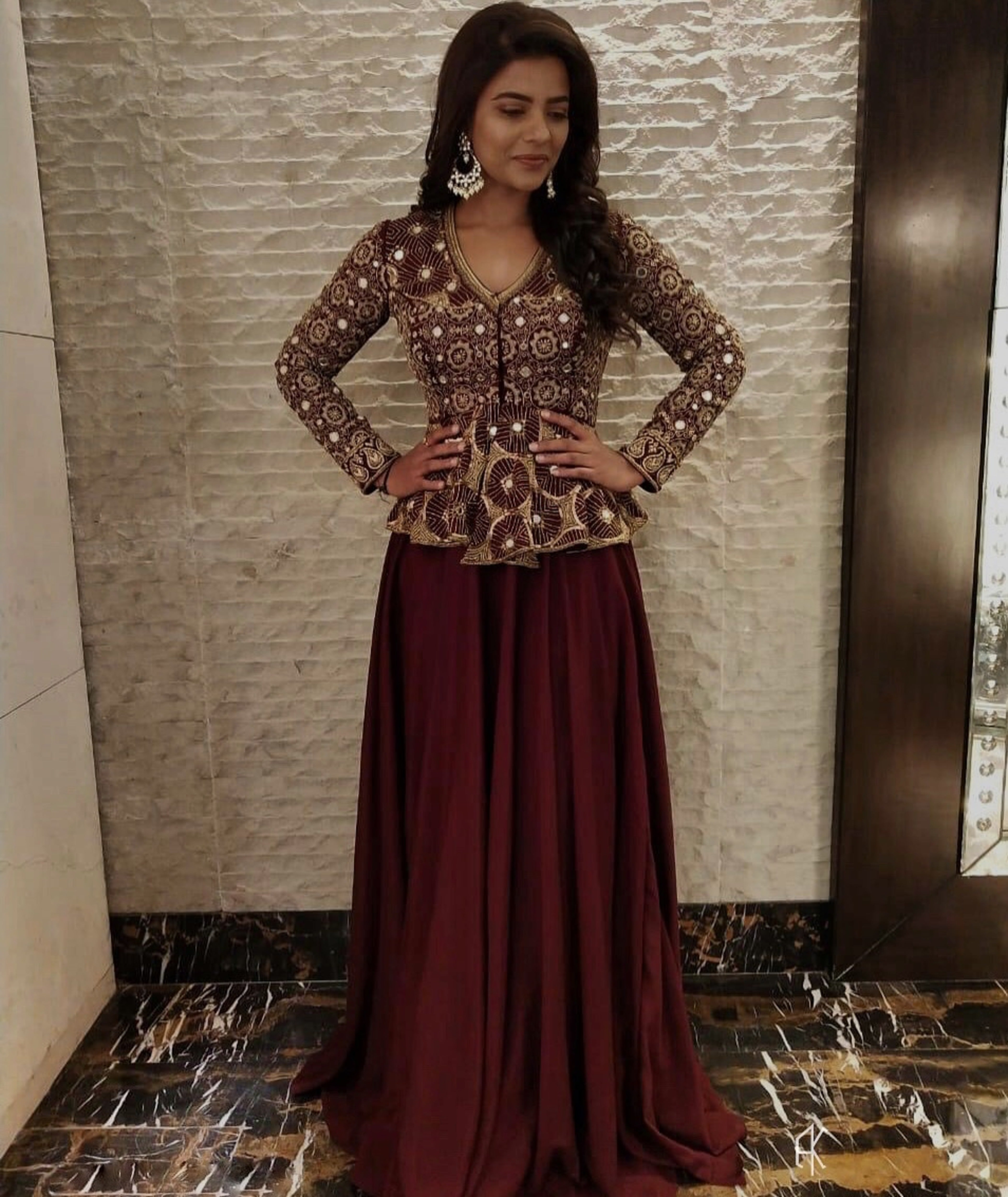 Actress Aishwarya Rajesh in a handcrafted peplum sharara in wine red for the promo of the movie world famous lover with vijay devarakonda. She is smiling looking down