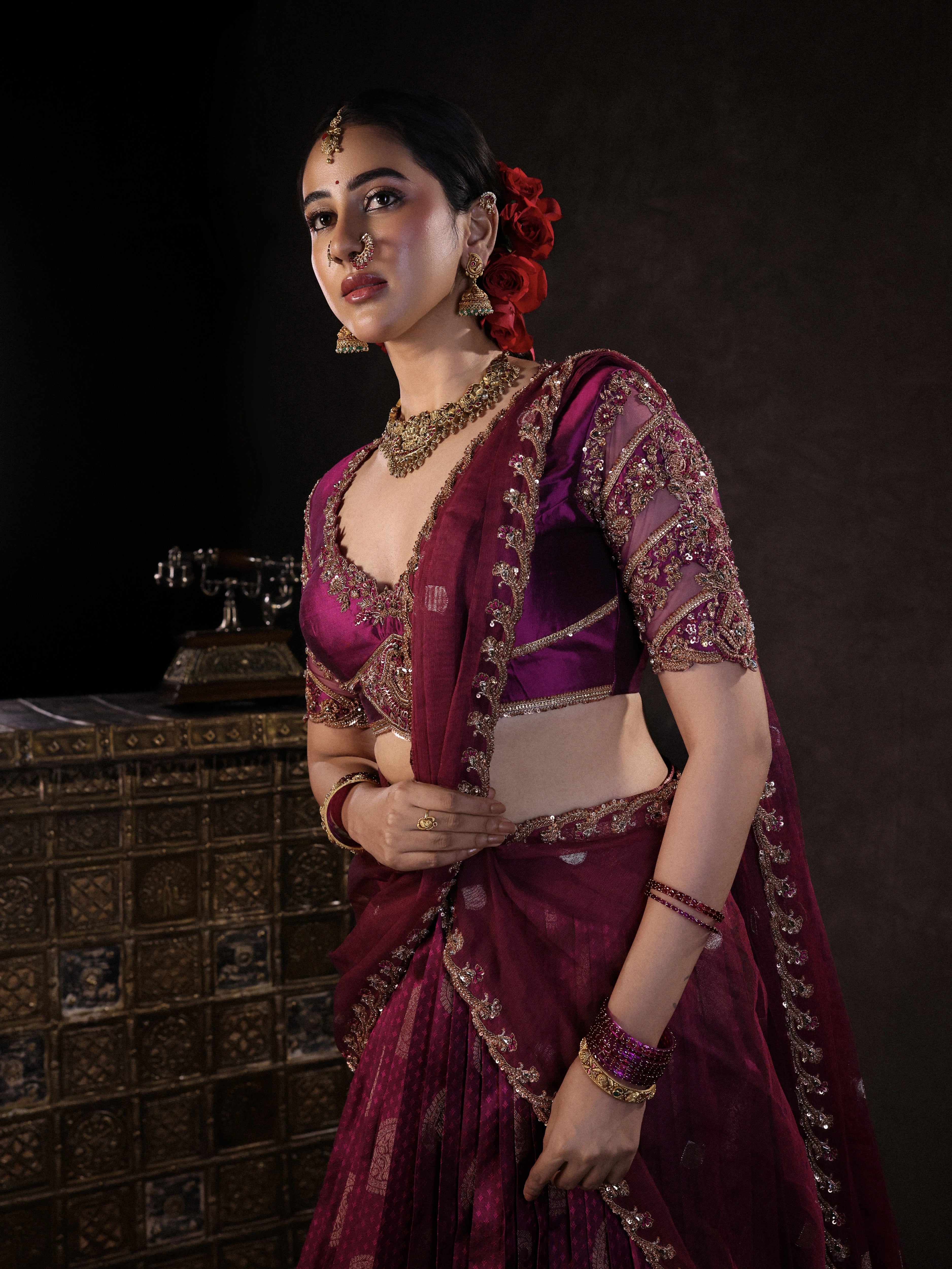 Actress Akshaya Hariharan posing in a dark magenta silk half saree set handcrafted with zardozi, resham, cutdana, sequins & rhinestones. Team Archana Karthick completed the style with dark magenta glass bangles, a ring, jhumkas, nose ring and a maang tikka.