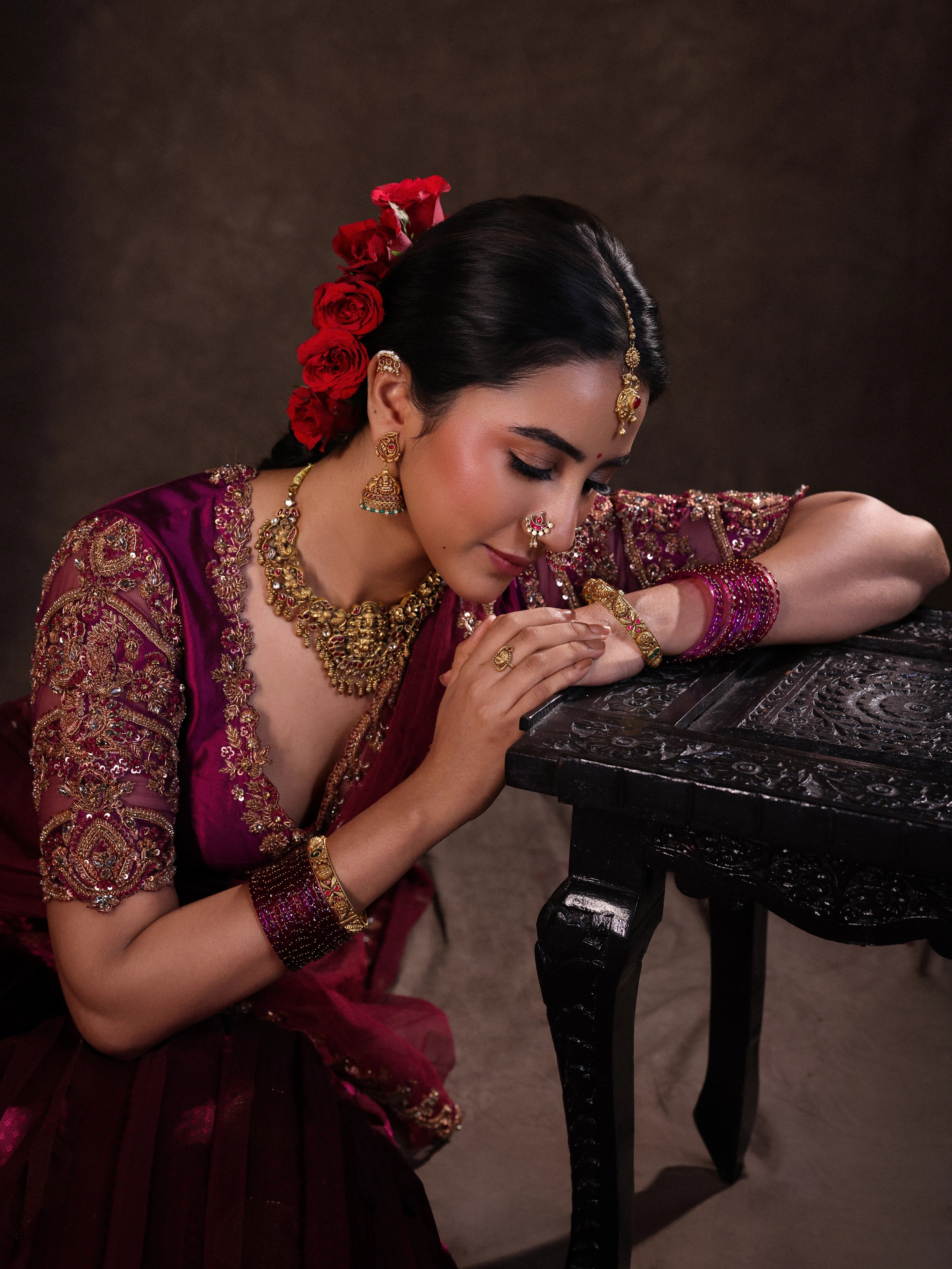 Actress Akshaya Hariharan posing seated in a dark magenta silk half saree set handcrafted with zardozi, resham, cutdana, sequins & rhinestones. Team Archana Karthick completed the style with dark magenta glass bangles, a ring, jhumkas, nose ring and a maang tikka.