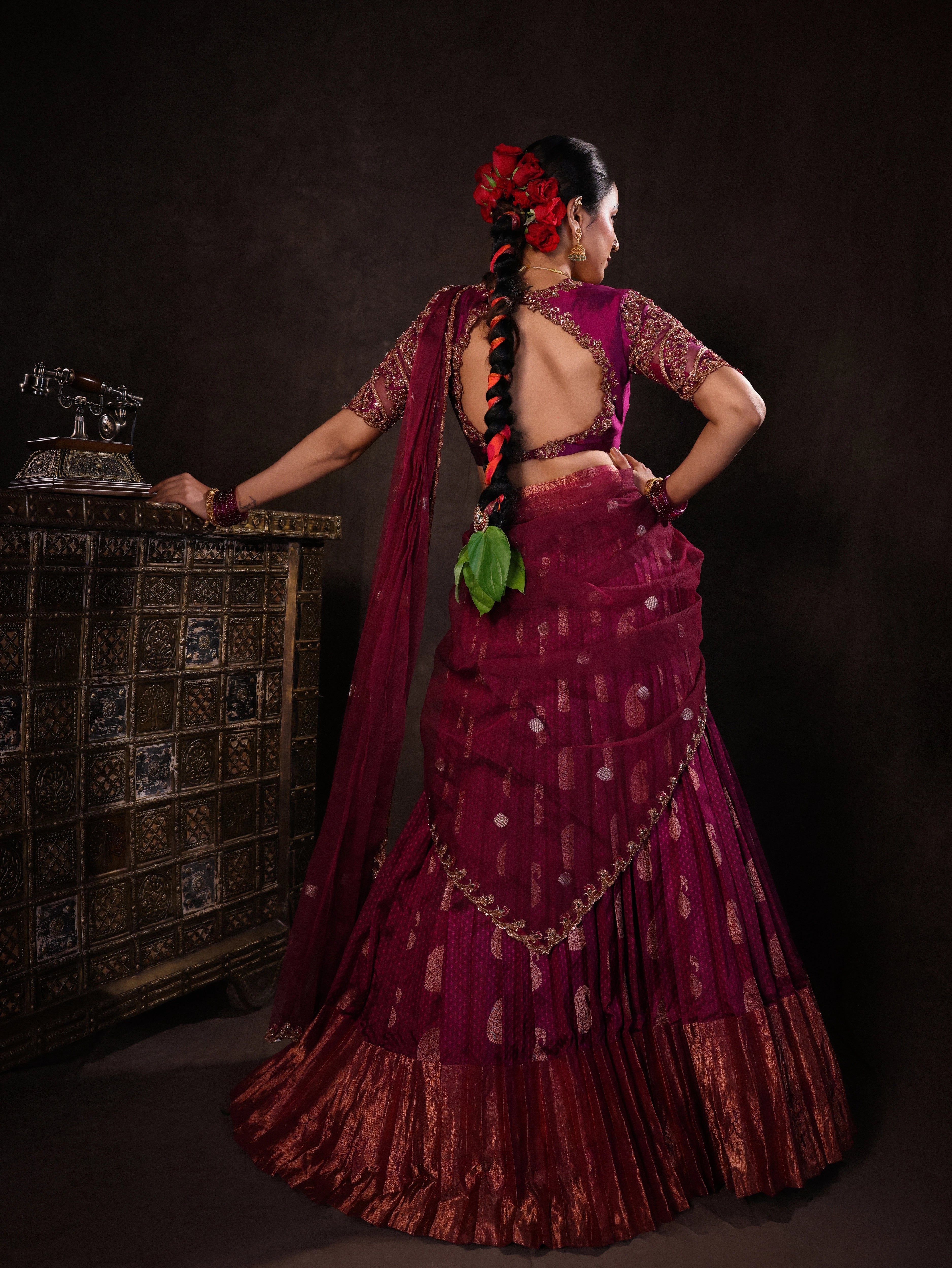 Actress Akshaya Hariharan showcasing back blouse design in a dark magenta silk half saree set handcrafted with zardozi, resham, cutdana, sequins & rhinestones. Team Archana Karthick completed the style with dark magenta glass bangles, a ring, jhumkas, nose ring and a maang tikka.