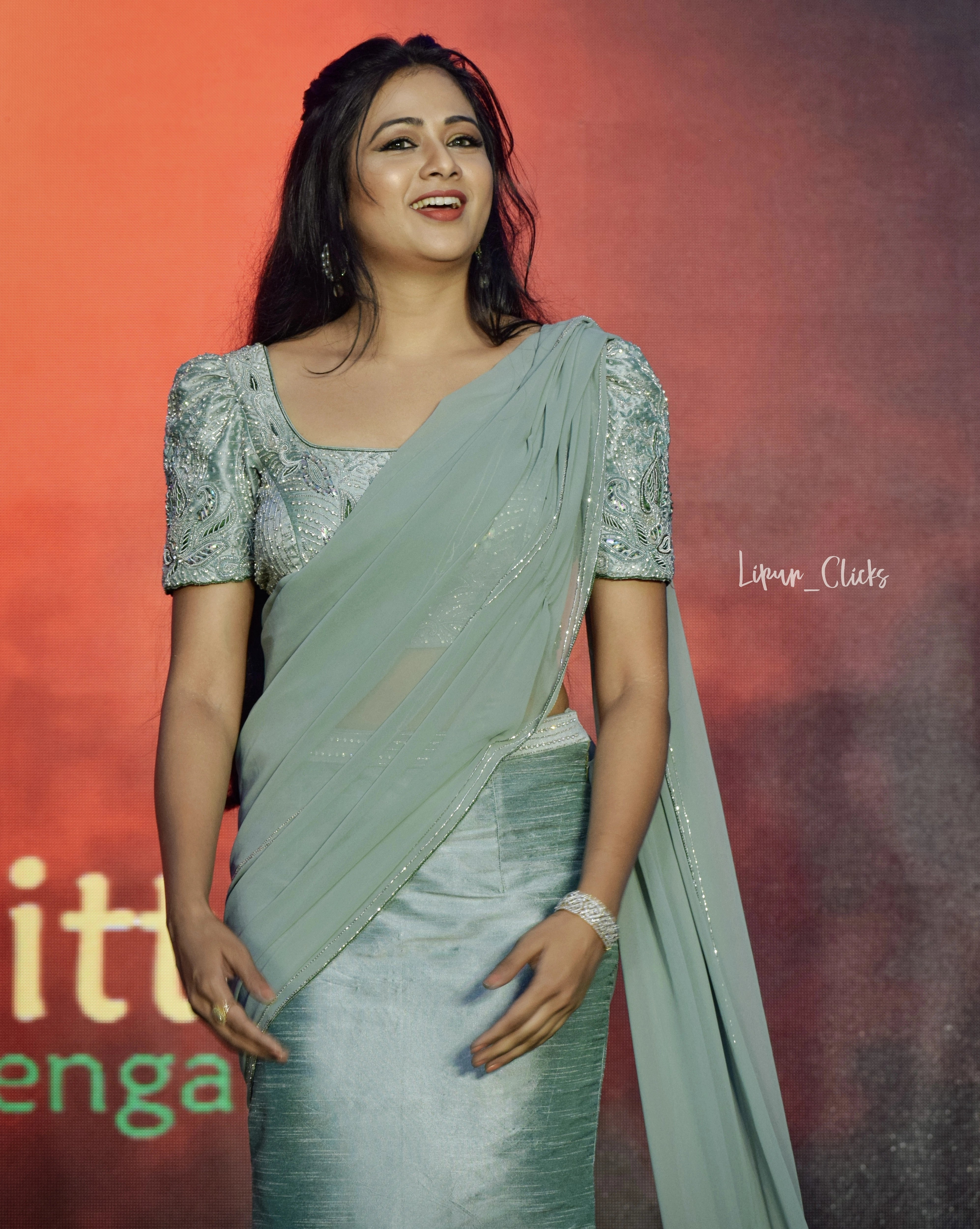Actress Archita Sahu smiling on stage in a light sea green georgette and raw silk draped mermaid lehenga with puff sleeves handcrafted by Archana Karthick.