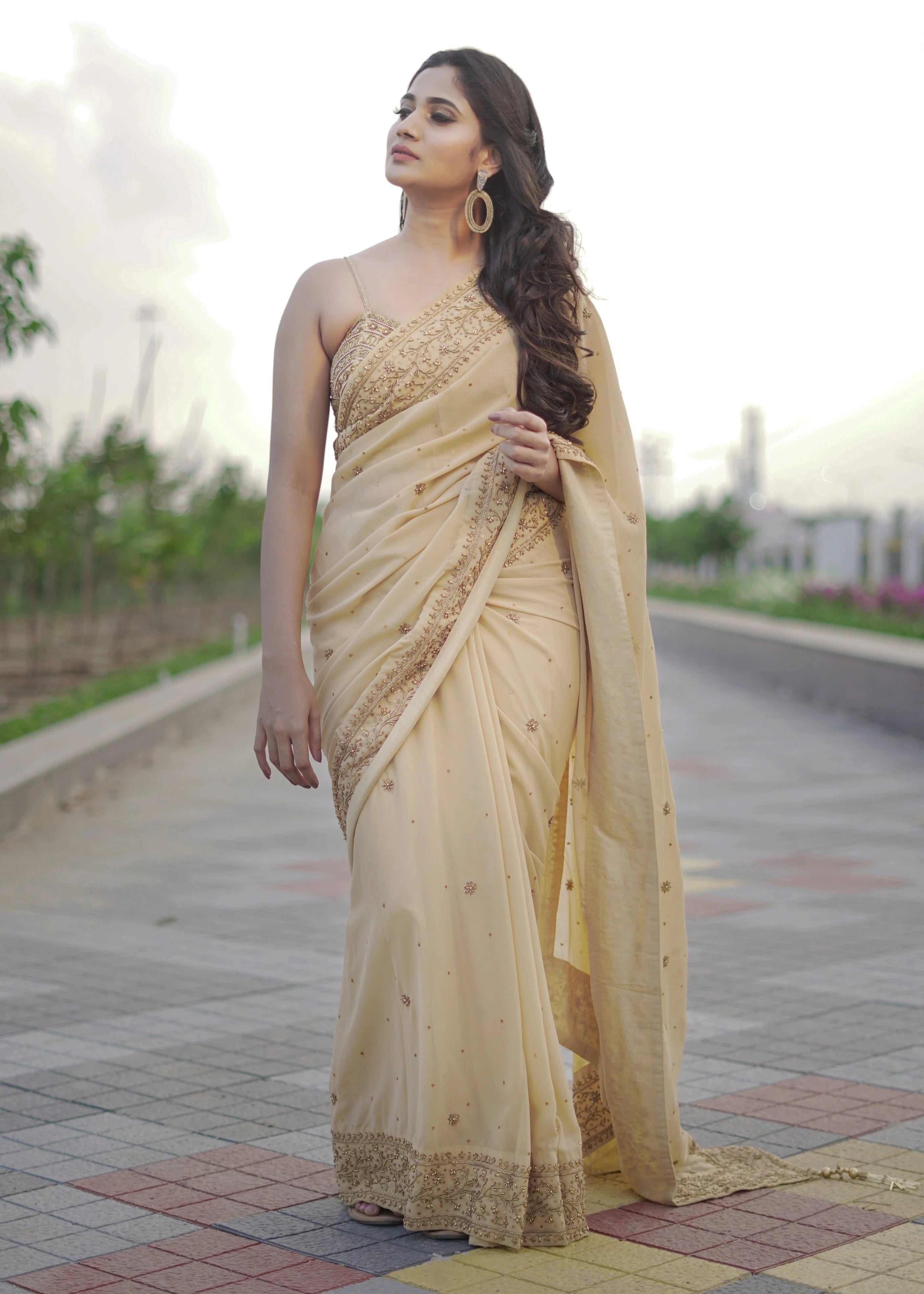 Actress & Bigg Boss fame Losliya posing in a beige georgette saree paired with a bralette, handcrafted with beads, sequins and pearls by team Archana Karthick.