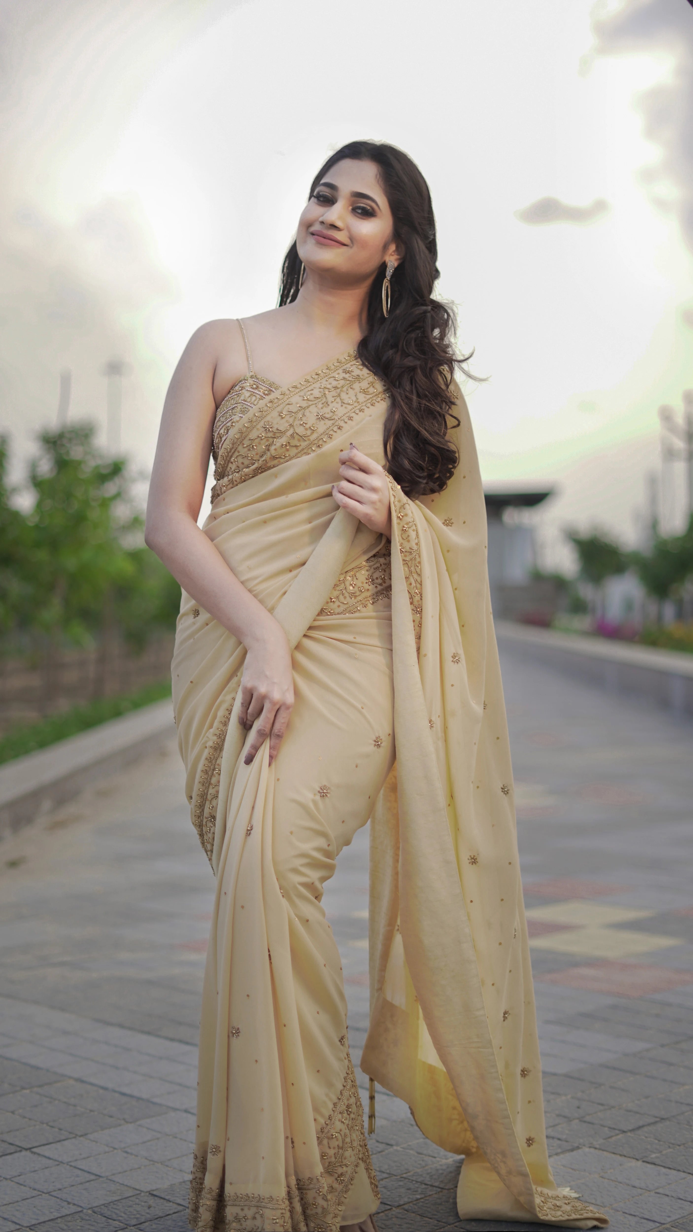 Actress & Bigg Boss fame Losliya smiling in a beige georgette saree paired with a bralette, handcrafted with beads, sequins and pearls by team Archana Karthick.